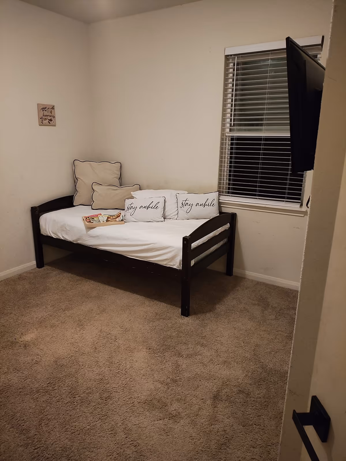 Small bedroom with a dark daybed, white linens, and a window with blinds.