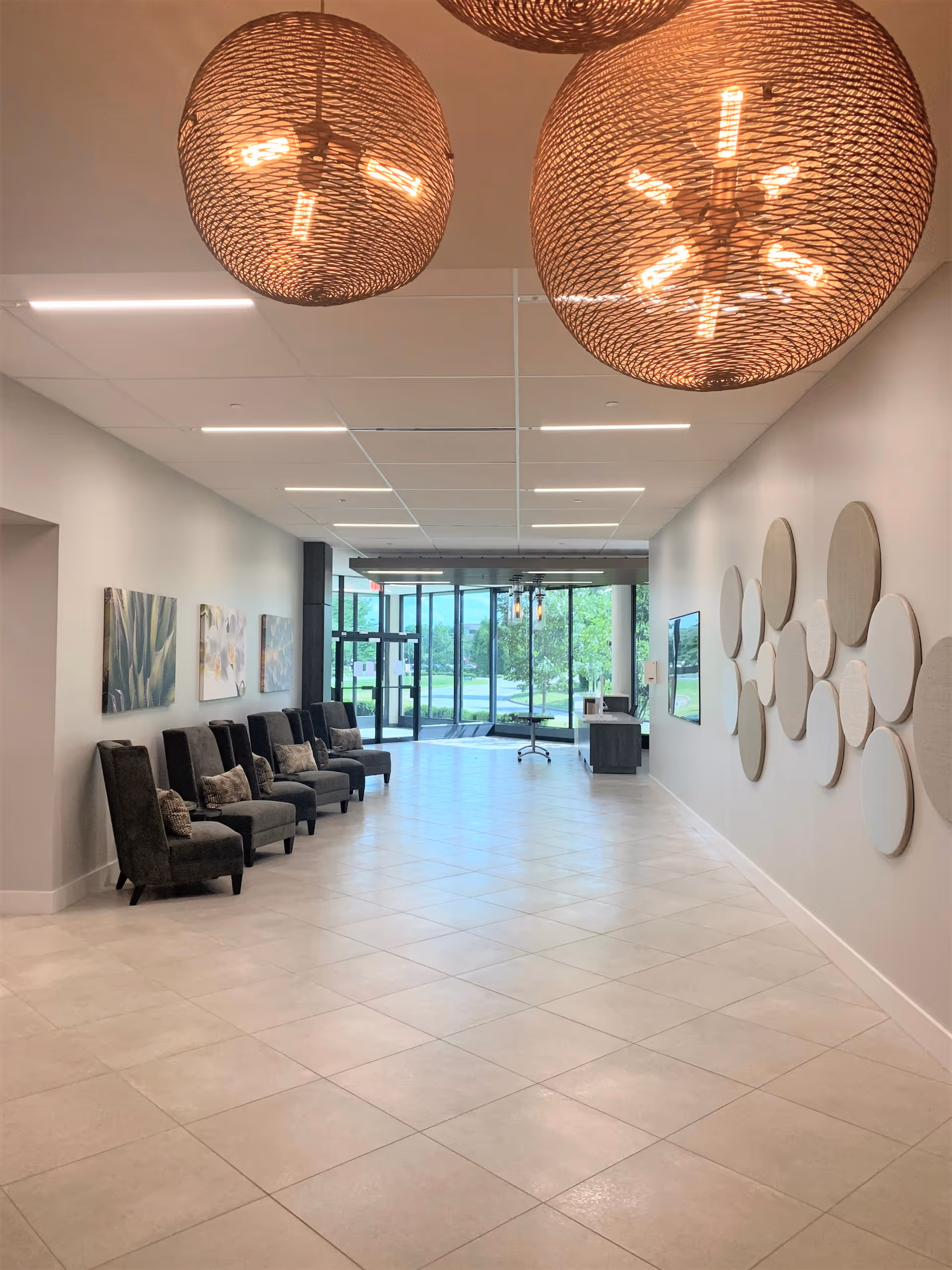 Bright interior lobby with multiple chairs along the left, decorative wall art, and glass doors.