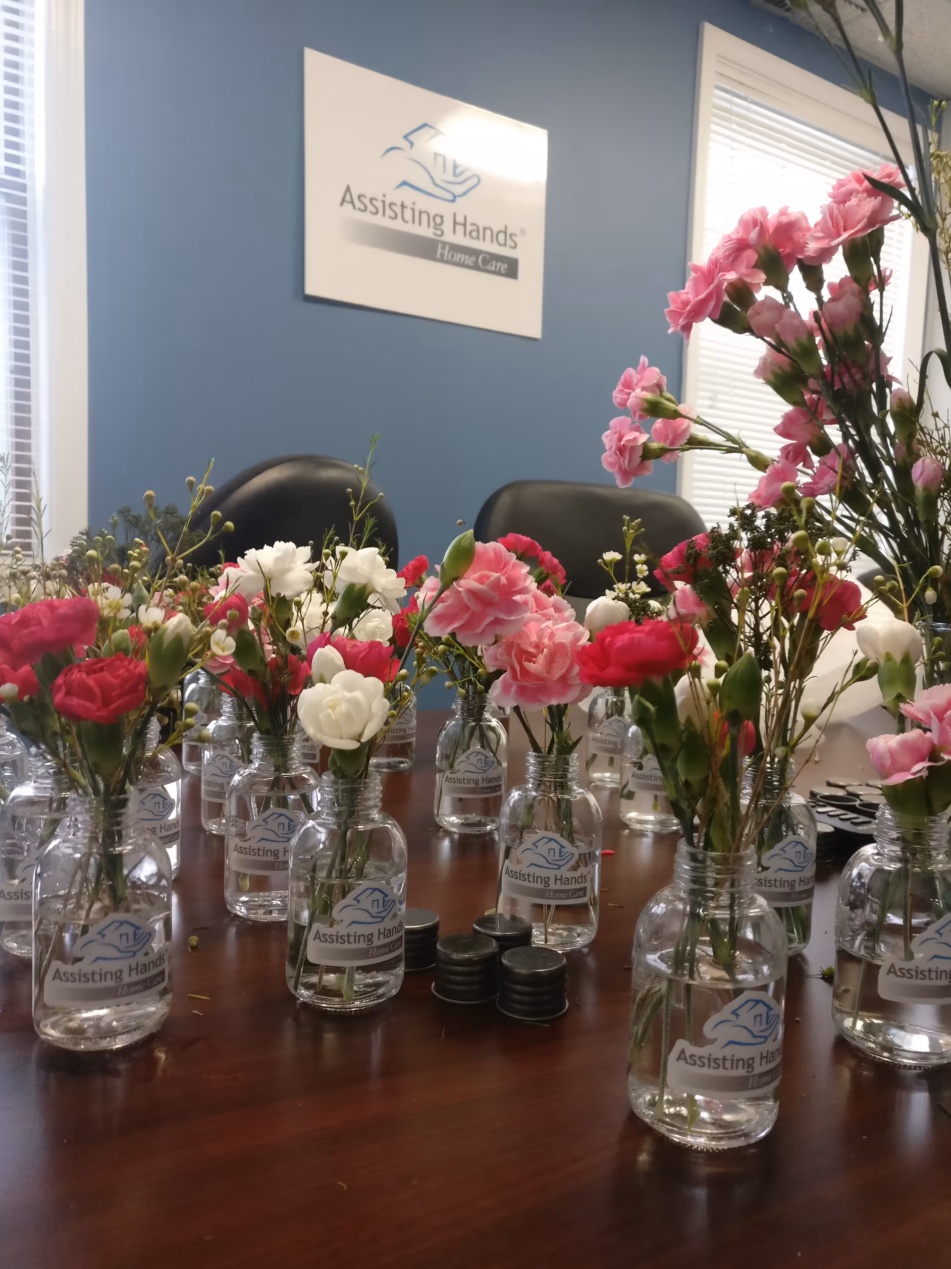 Interior meeting room with numerous glass vases of pink and white flowers on a table.