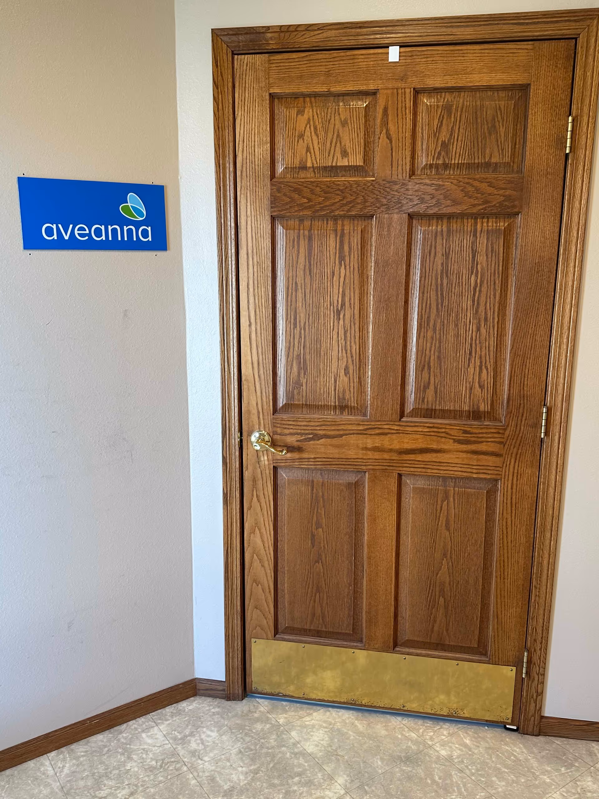 Wooden interior door with brass handle beside a blue Aveanna sign.