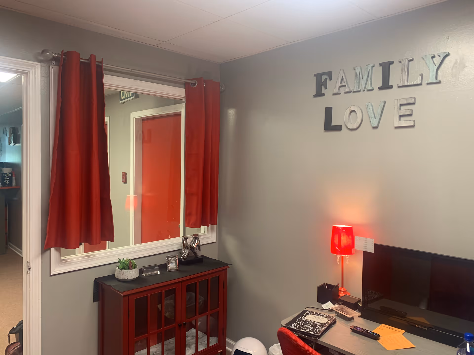 Interior reception area with red curtains, desk, computer, and 'FAMILY LOVE' wall decor.