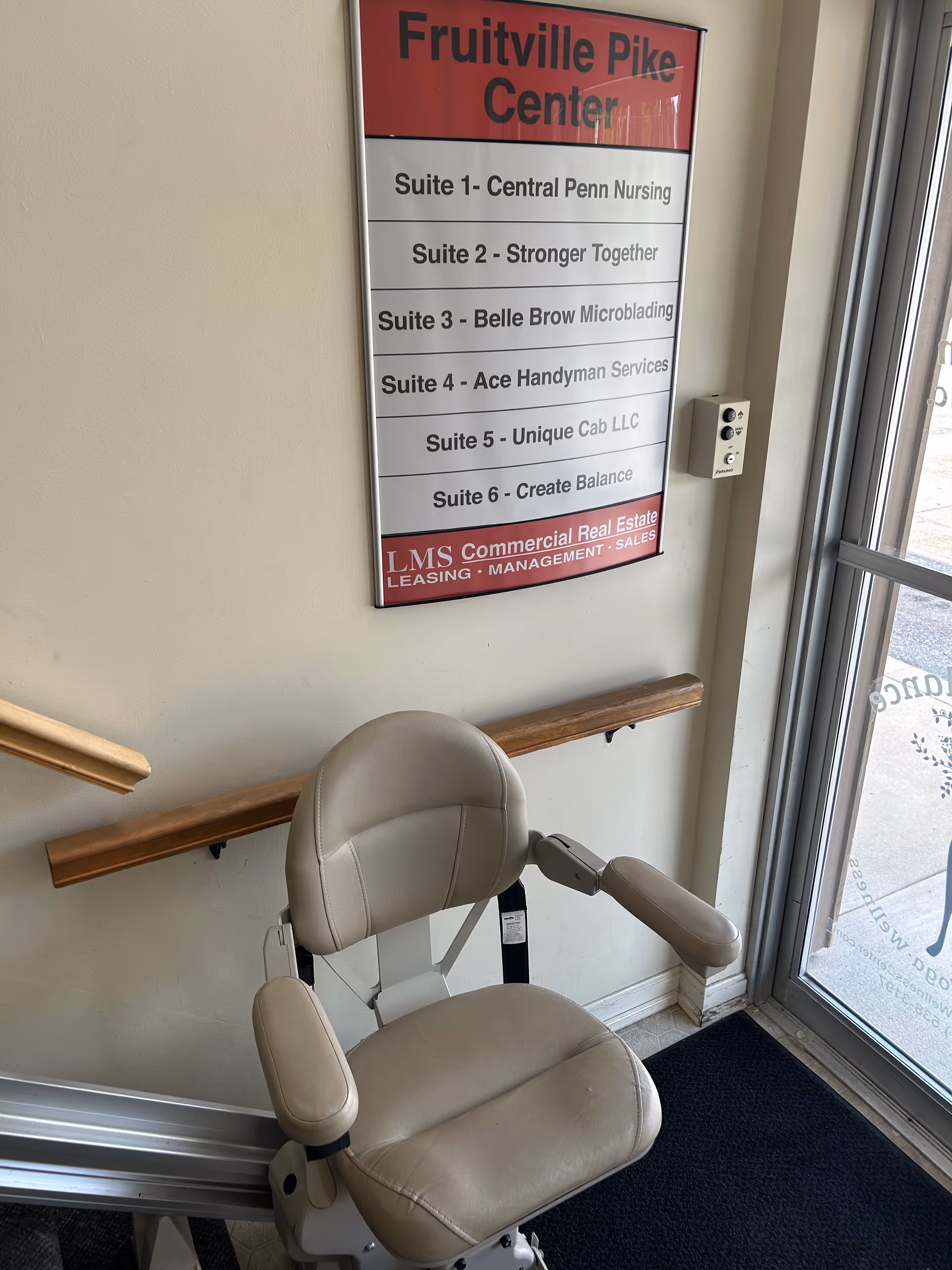 Interior hallway with beige chair beside a sign listing suites at Central Penn Nursing