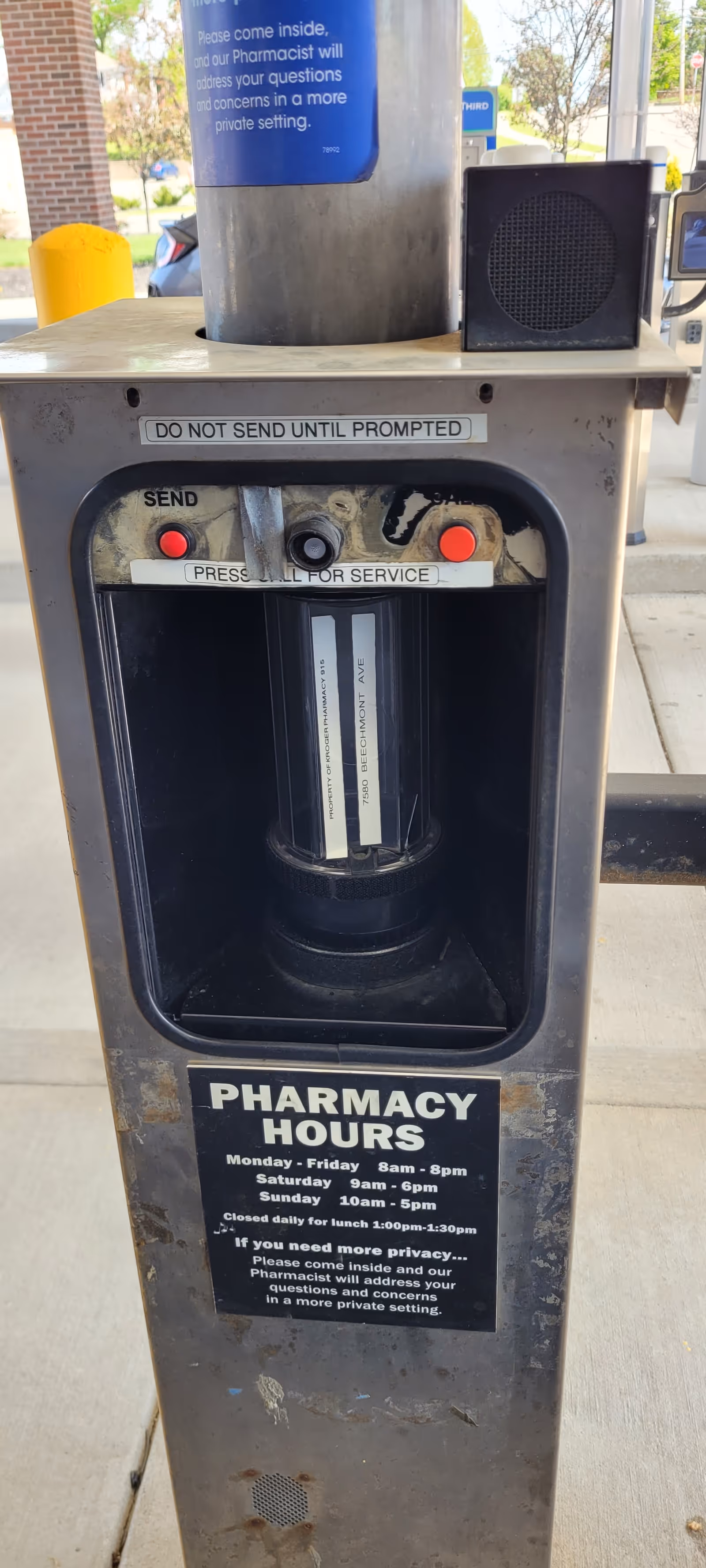 Outdoor Kroger Pharmacy kiosk with service buttons and hours sign beside brick column.