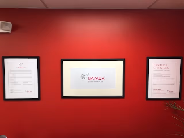 Red wall with three framed documents, center frame displays BAYADA Home Health Care logo.