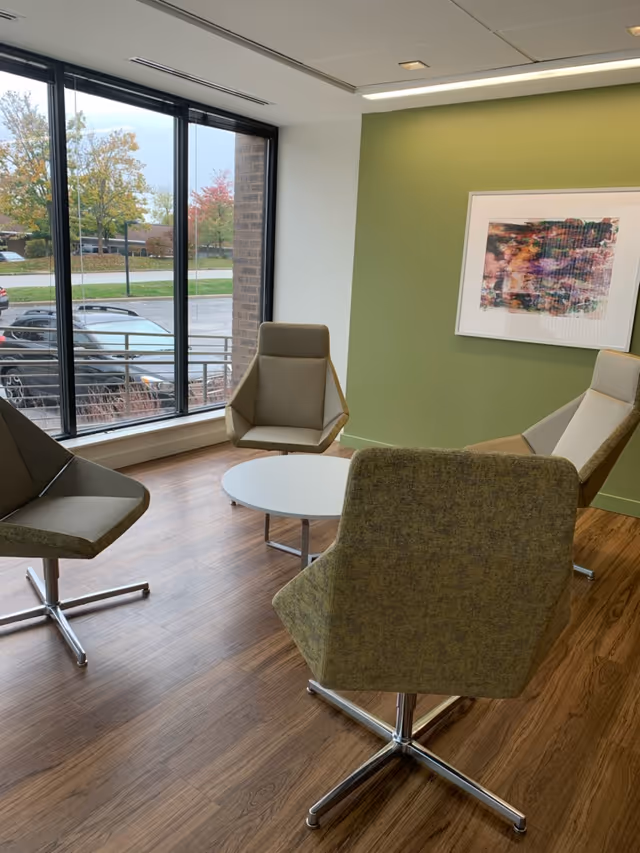 Modern lounge with four armchairs around a circular table by large windows.