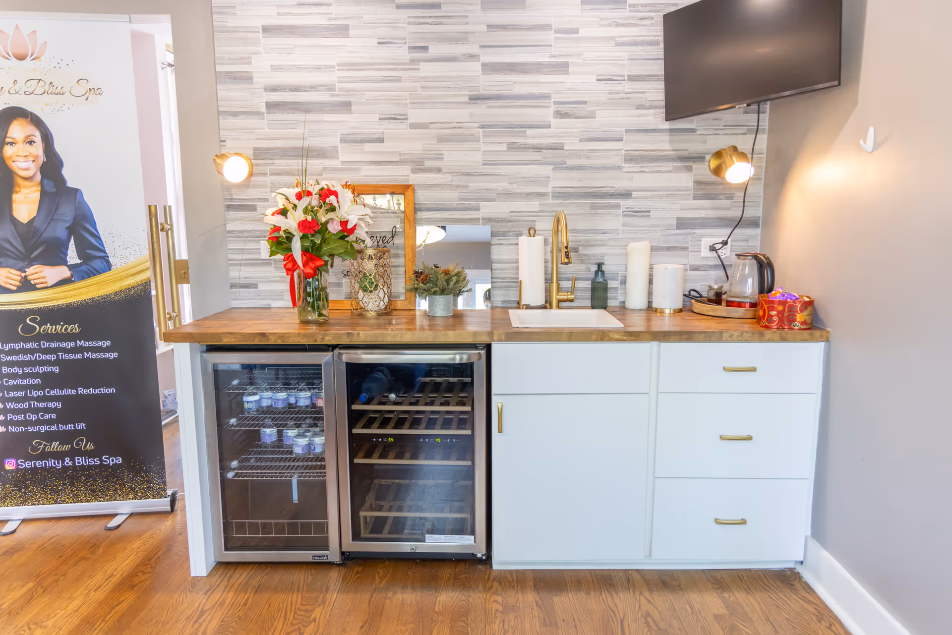 Compact kitchenette with sink, mini-fridge, coffee maker, flowers, and wall-mounted TV.