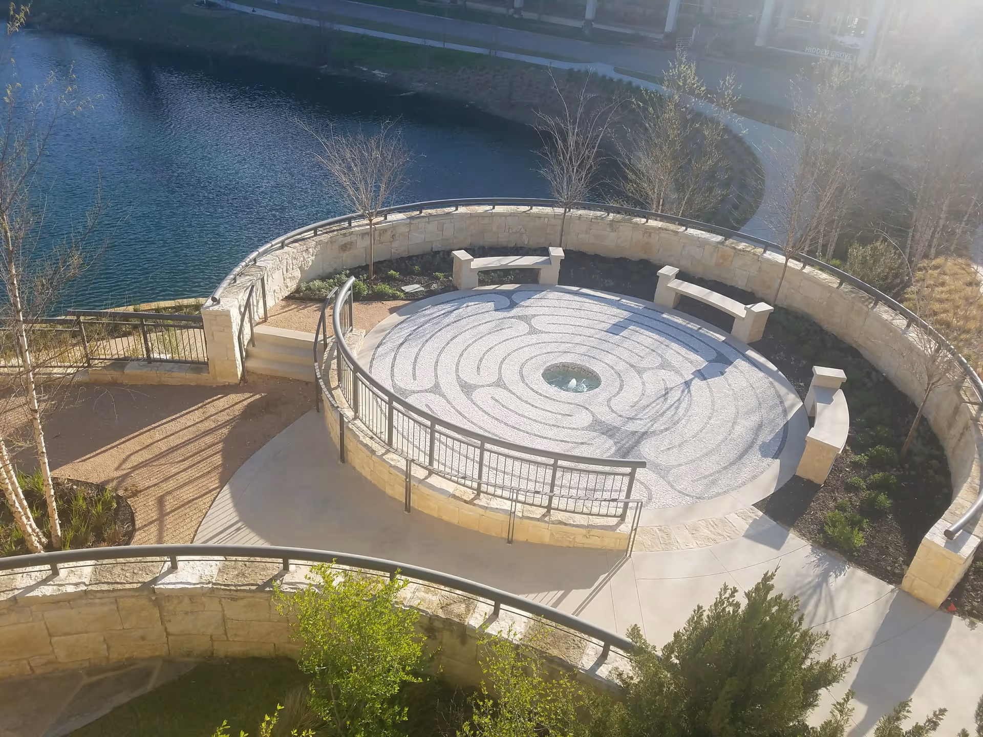 Circular stone courtyard with benches around a fountain beside a waterway.