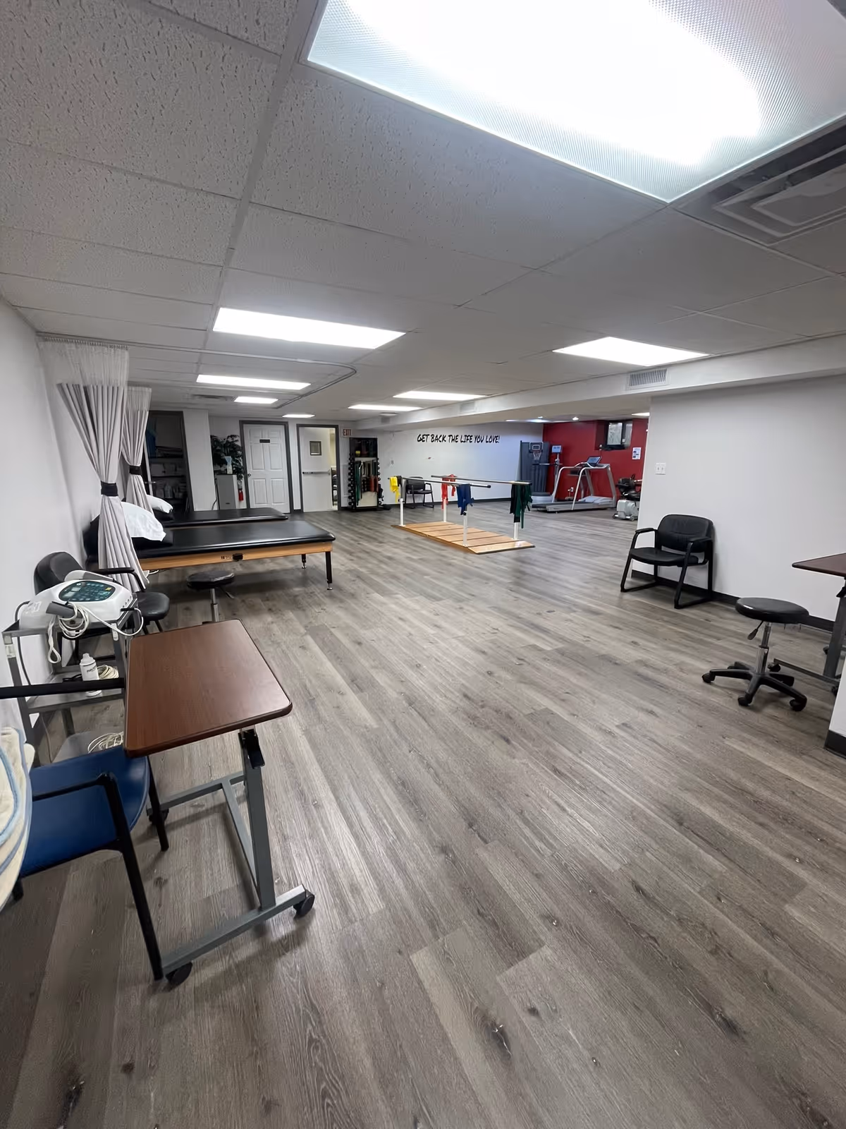 Rehabilitation therapy room with parallel bars, treatment tables, and exercise equipment.