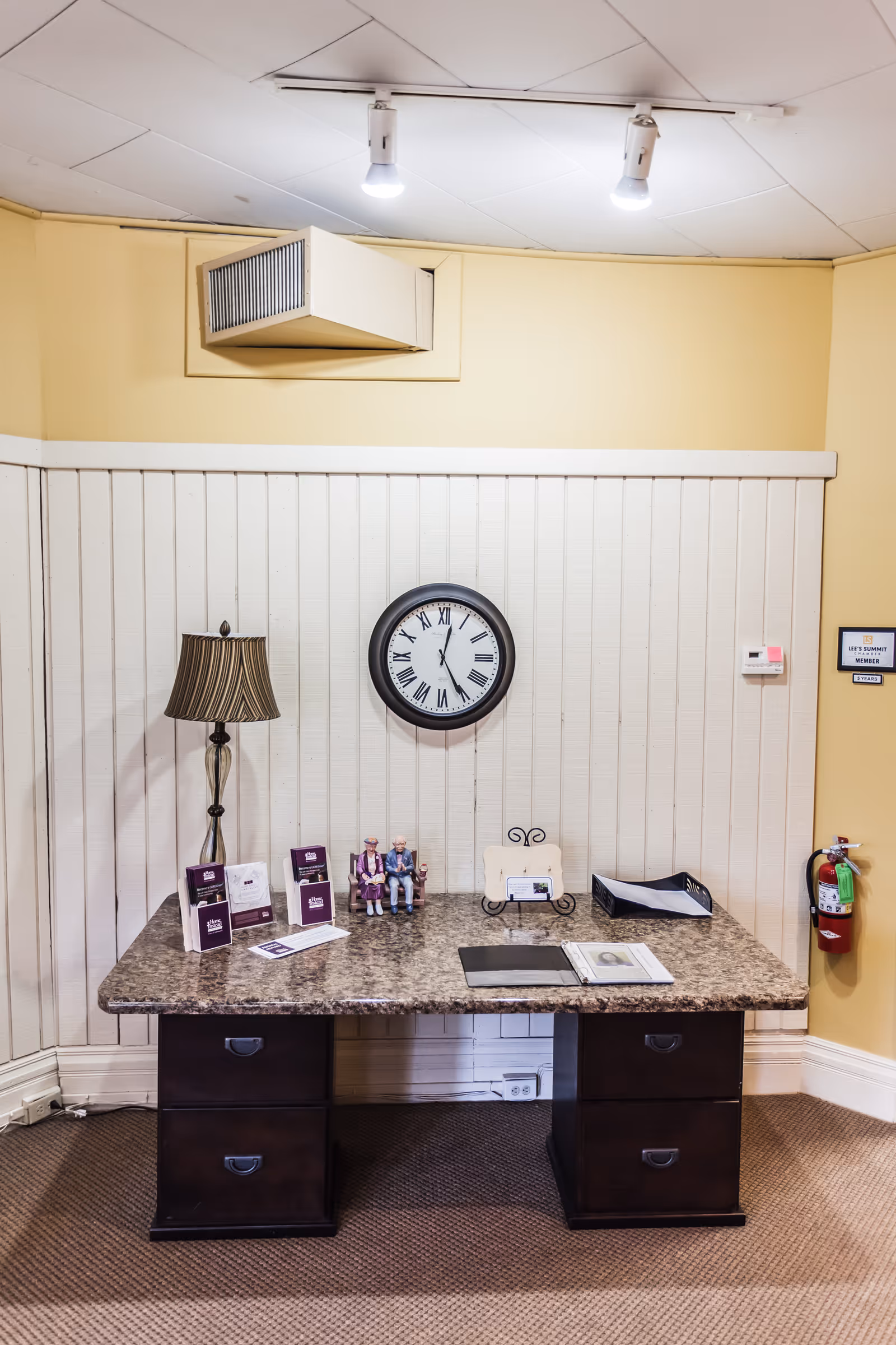 A desk with a wall clock, lamp, and brochures in a reception area.