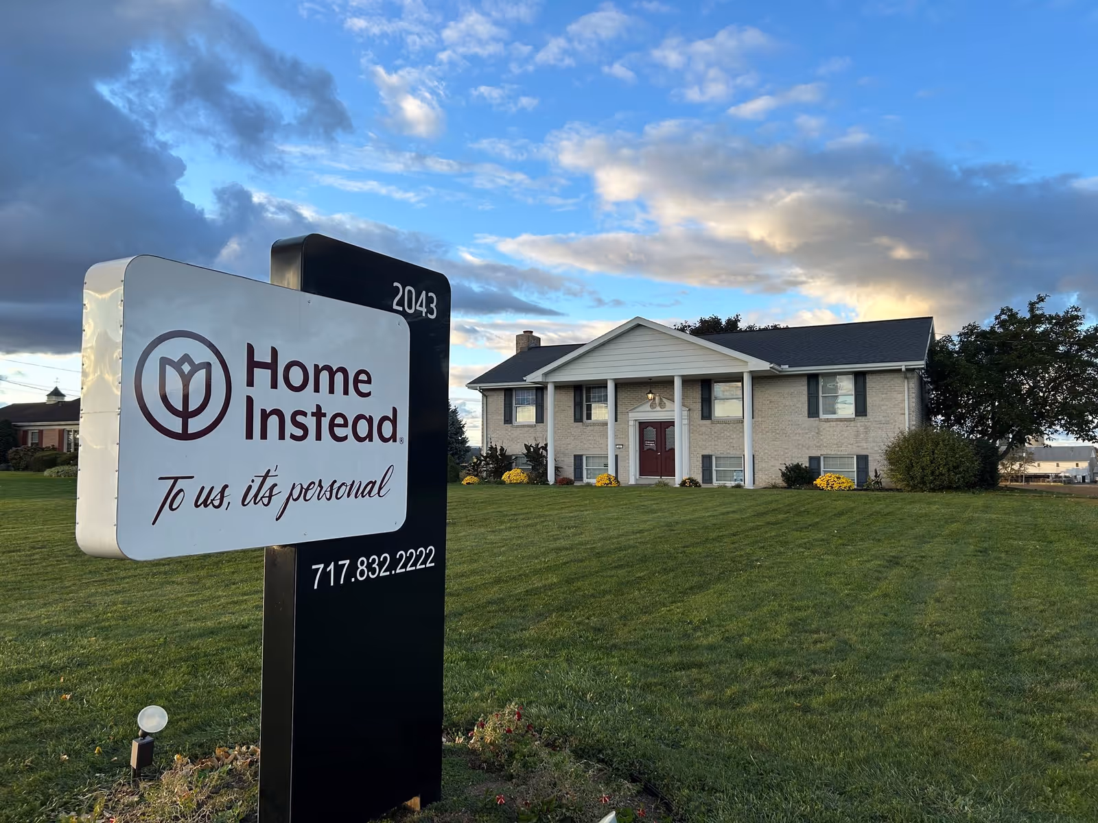 A Home Instead sign in the foreground with a two-story brick building behind