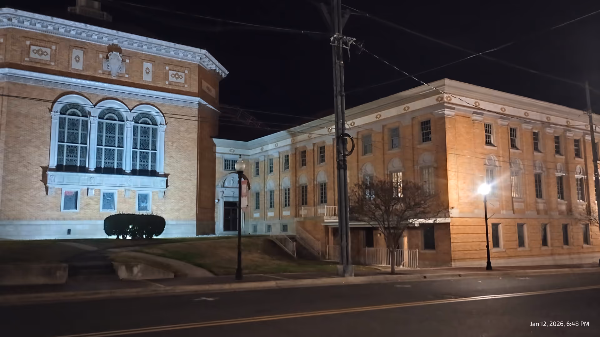 Nighttime exterior view of a brick senior living facility with arched windows and lit street lamps.
