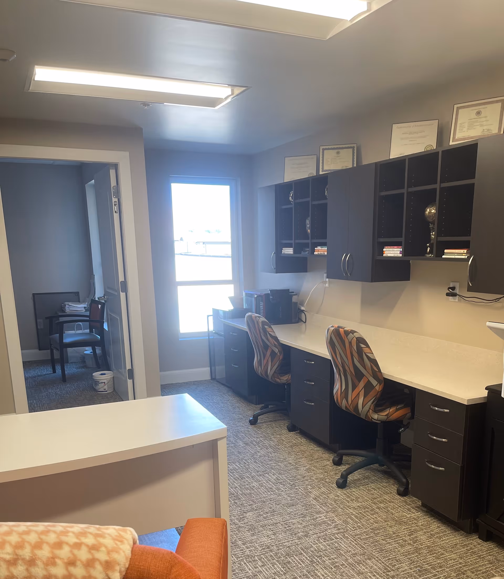 Office workspace in a senior facility with desks, chairs, cabinets, and certificates.
