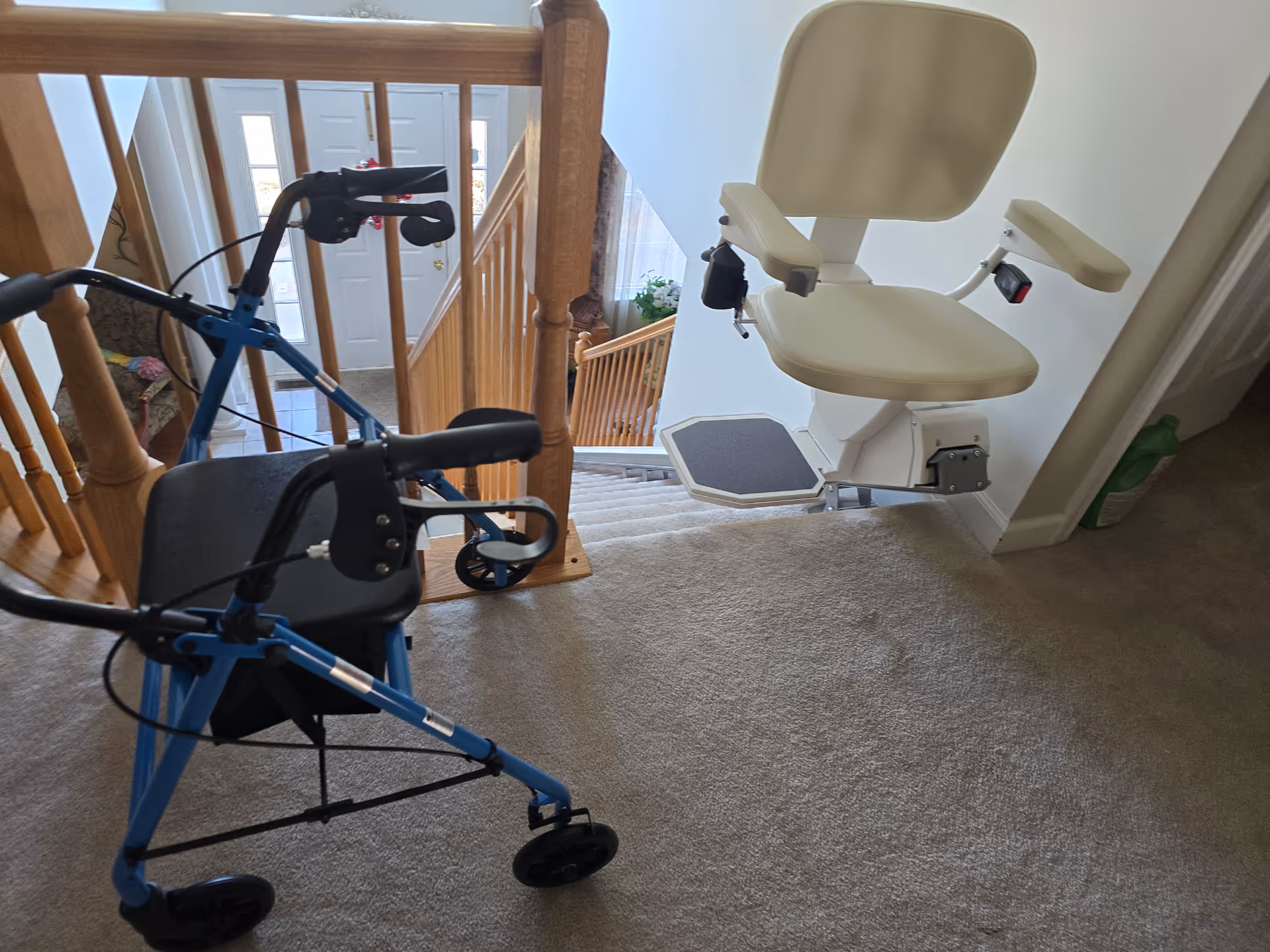 Blue rollator walker beside a white stair lift chair on a carpeted staircase landing.