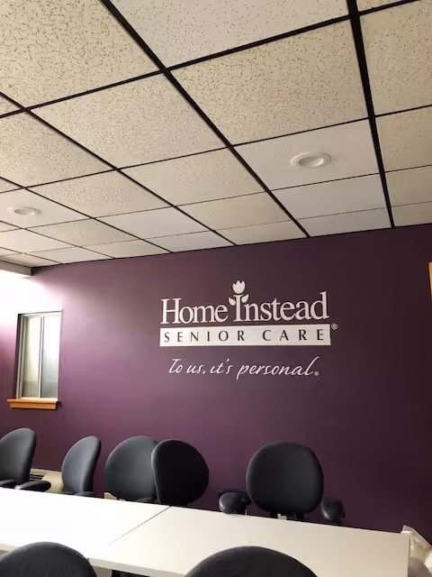 Purple wall with Home Instead Senior Care logo and row of chairs in reception area.