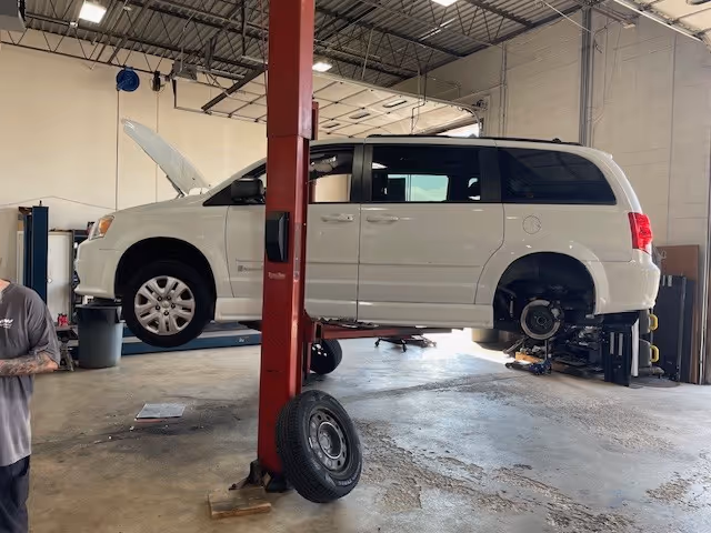 White minivan elevated on a hydraulic lift inside a repair shop.