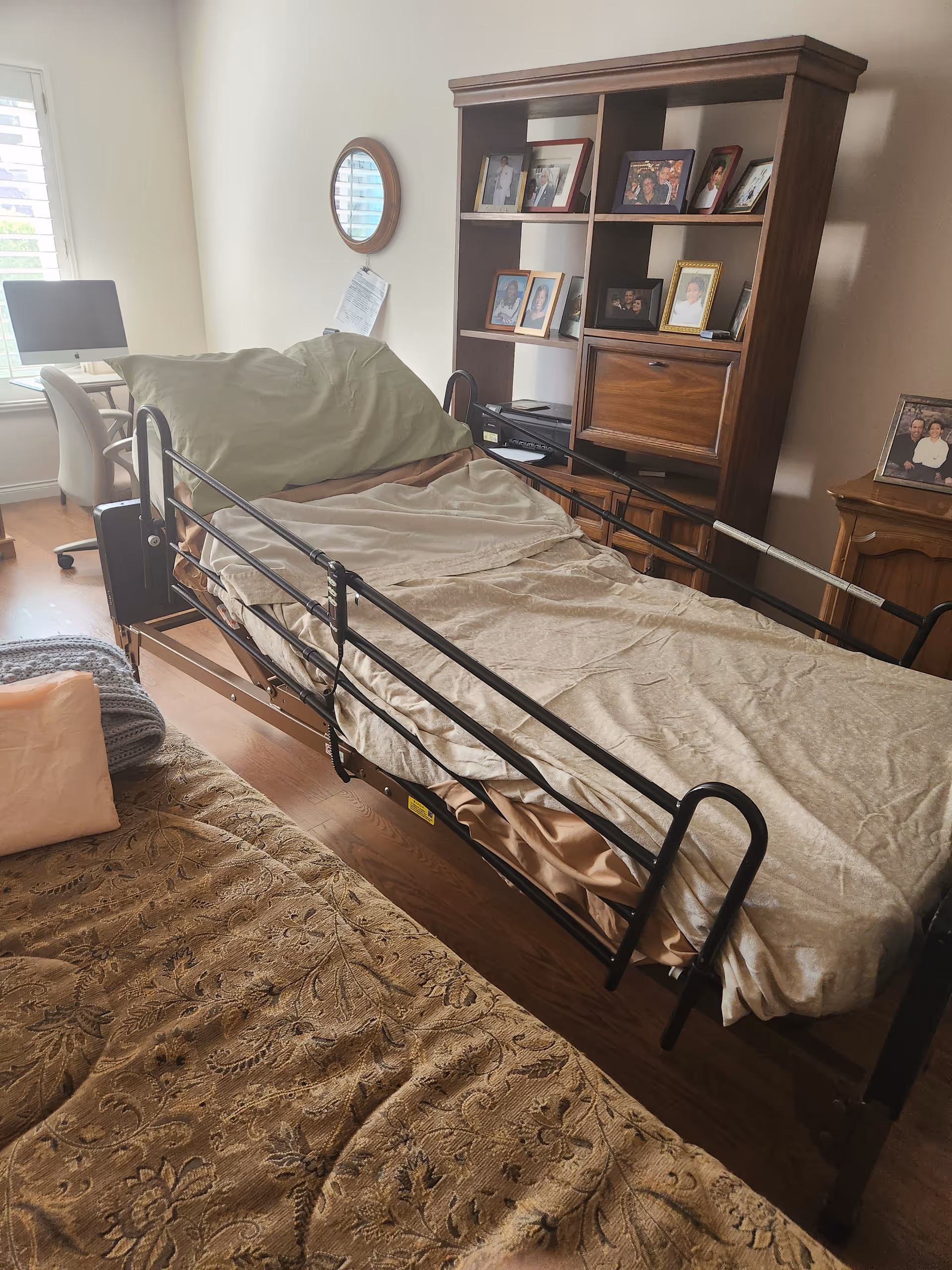 Hospital-style adjustable bed in a bedroom with photos and a desk.