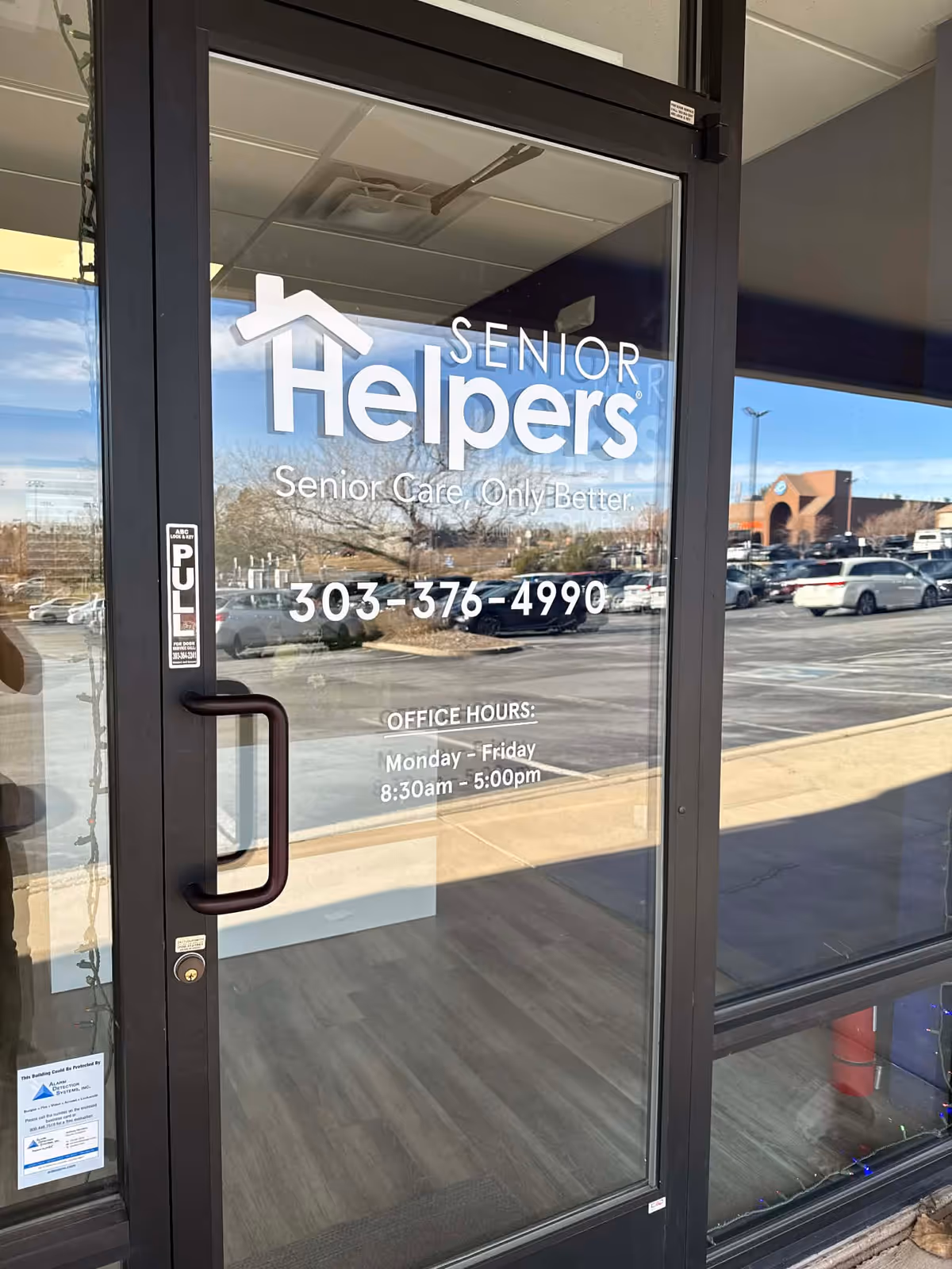 Glass entrance door with Senior Helpers branding and reflected parking lot outside.