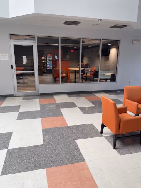 Indoor lounge area with orange chairs and a glass-walled room visible beyond.
