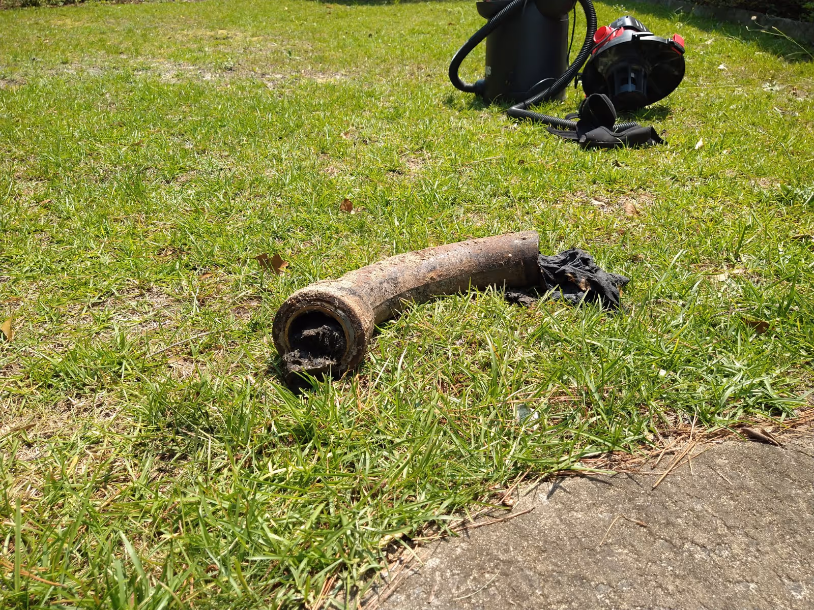 Rusty curved pipe and cloth lie on a grassy outdoor area near equipment.