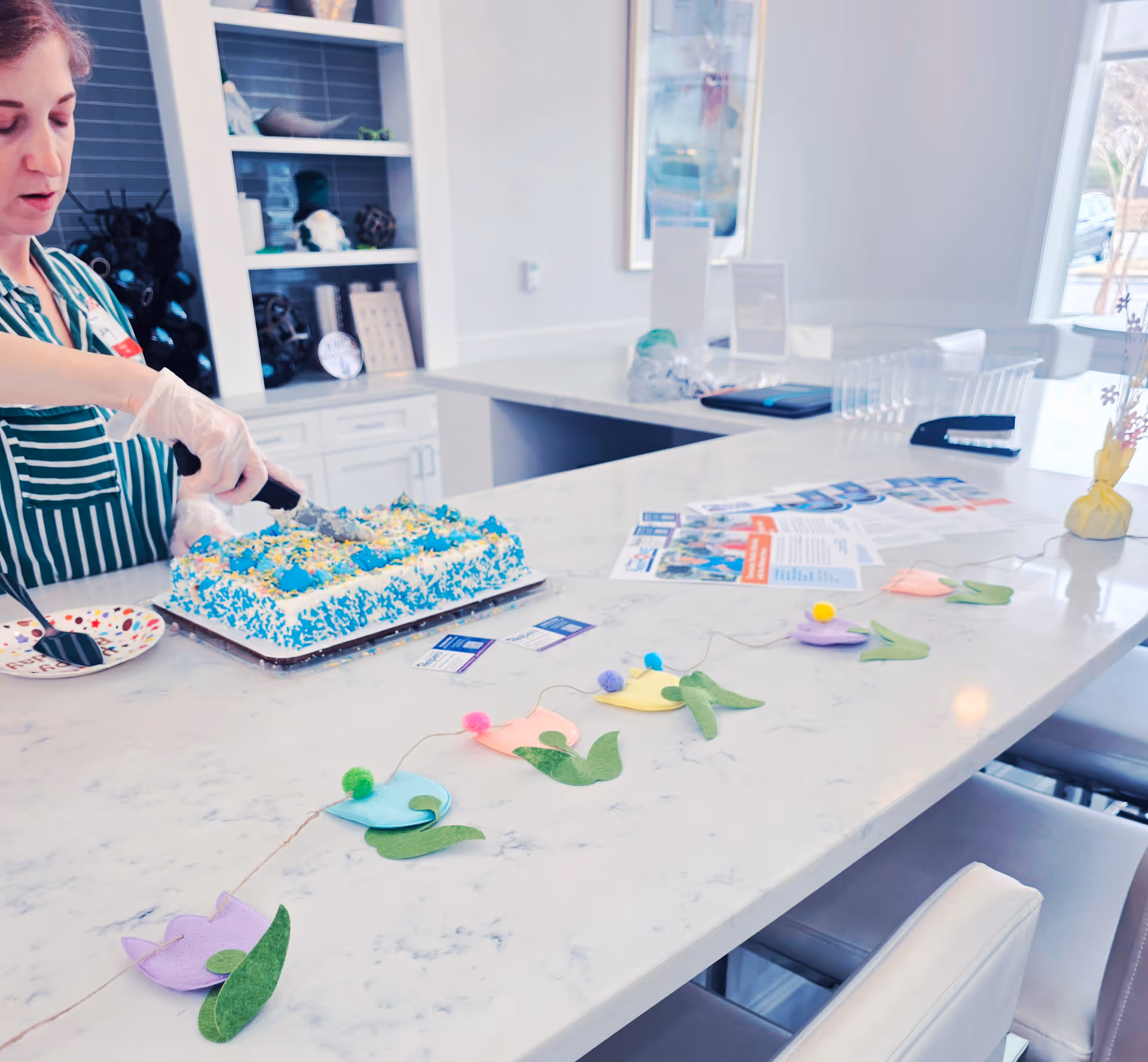 A caregiver decorates a cake at a marble kitchen island in a senior living facility.