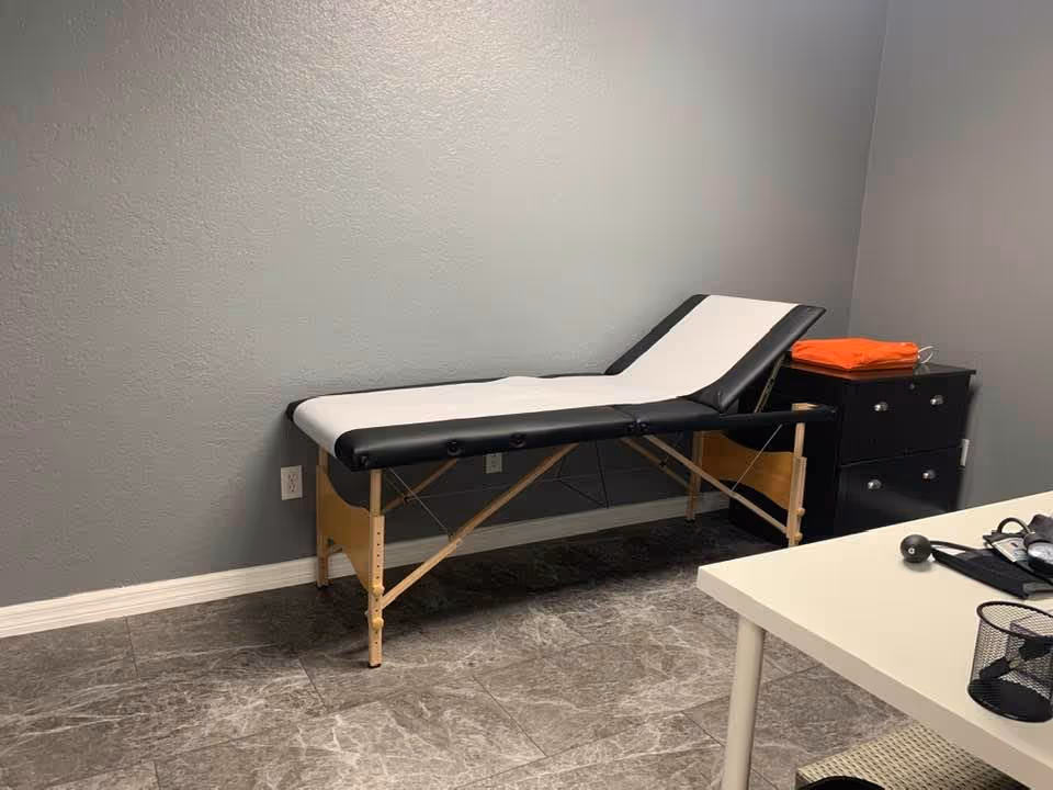 Exam table along gray wall in a small, basic clinic or exam room.