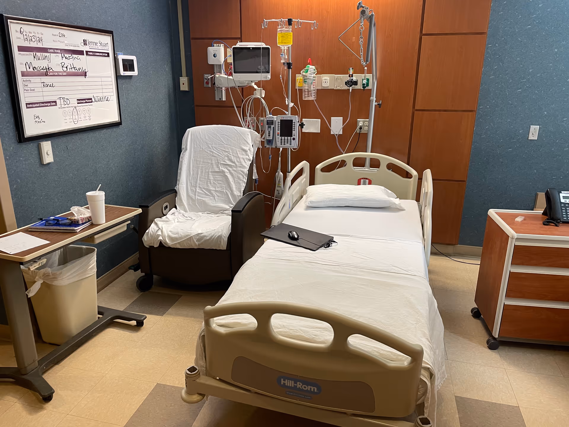 Hospital patient room with a bed, chair, monitors, and IV equipment.