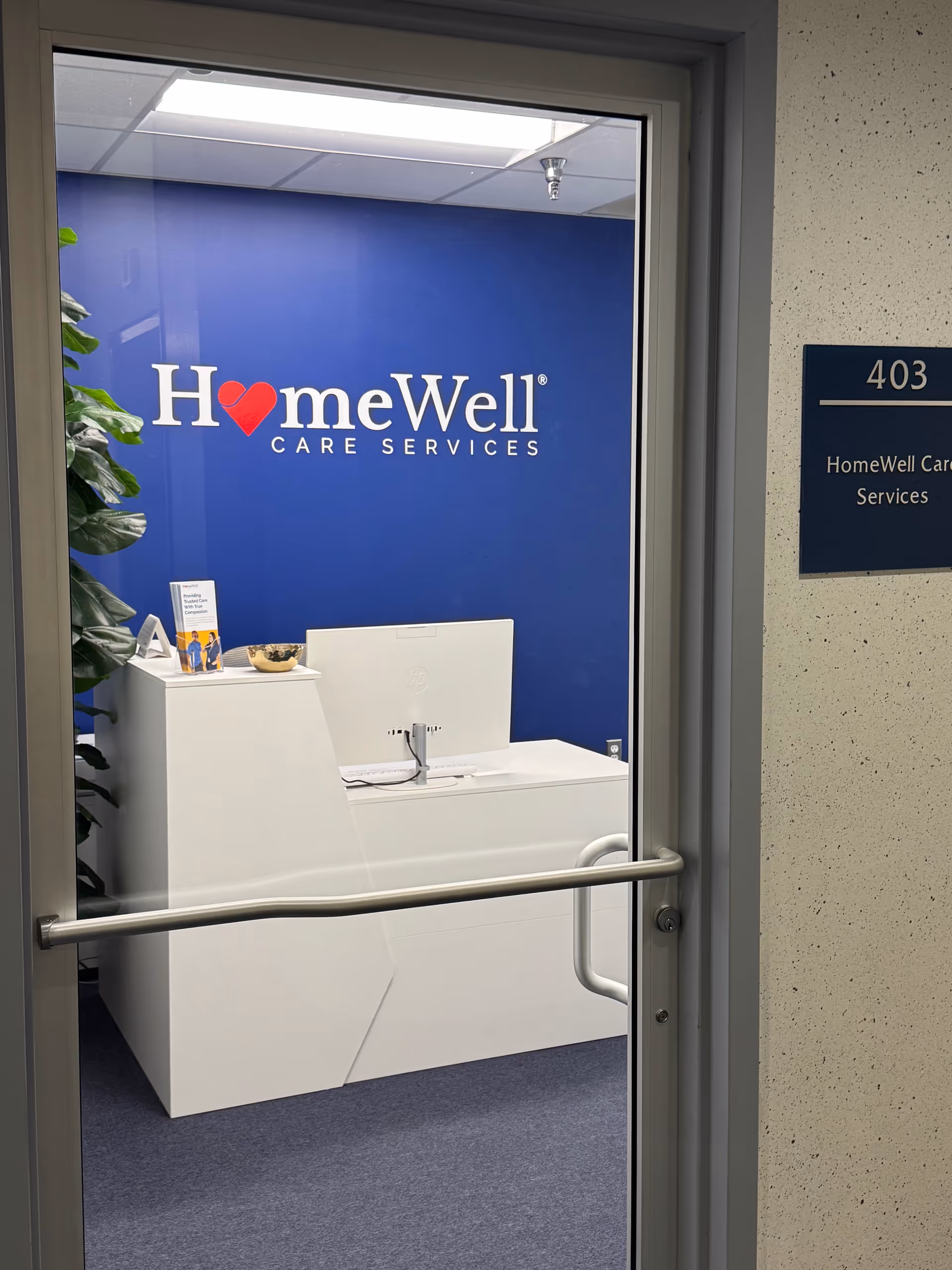 Blue HomeWell Care Services signage on blue wall behind a white reception desk in an office.