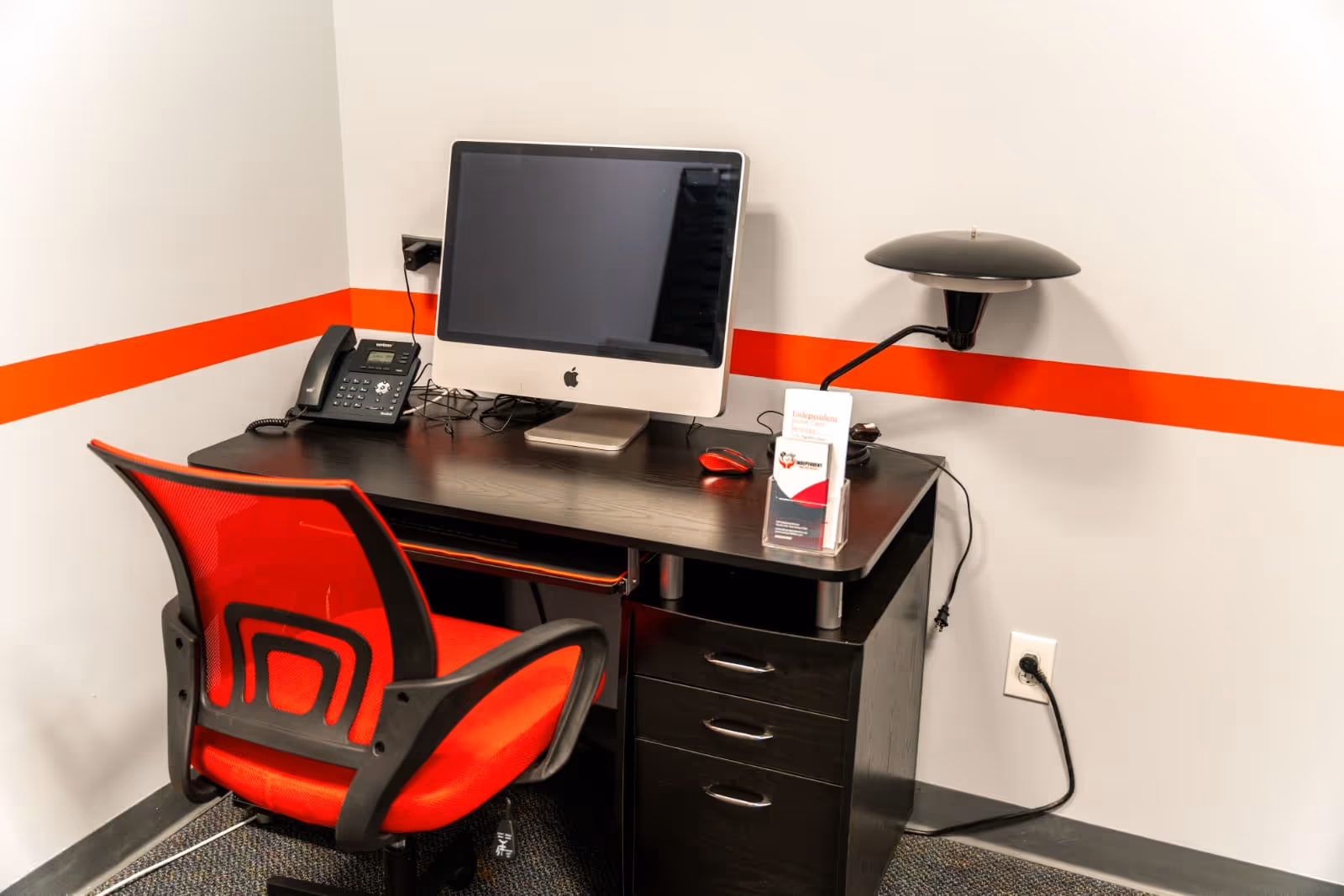 Desk setup with computer, red chair, and orange wall stripe.