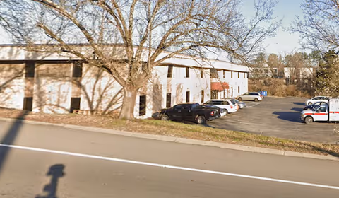 Exterior view of a facility with parked cars, leafless trees, and a road in foreground.