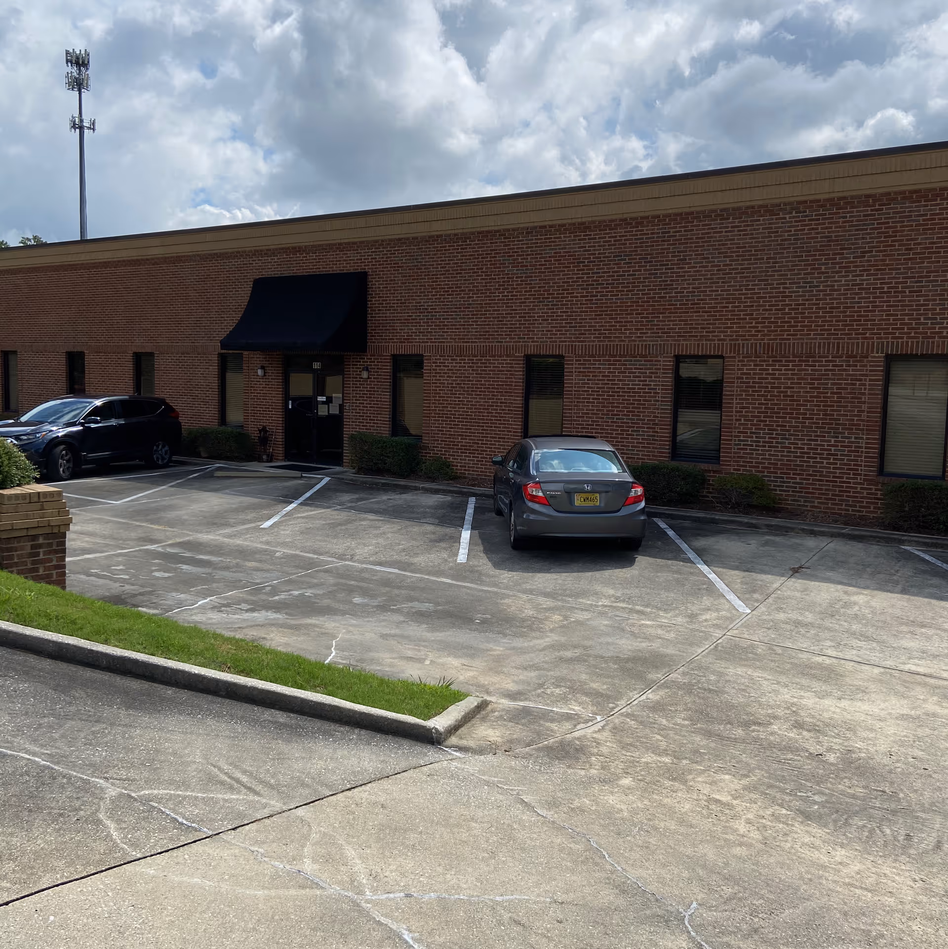 Brick building exterior with entrance, parking lot, and a dark awning.
