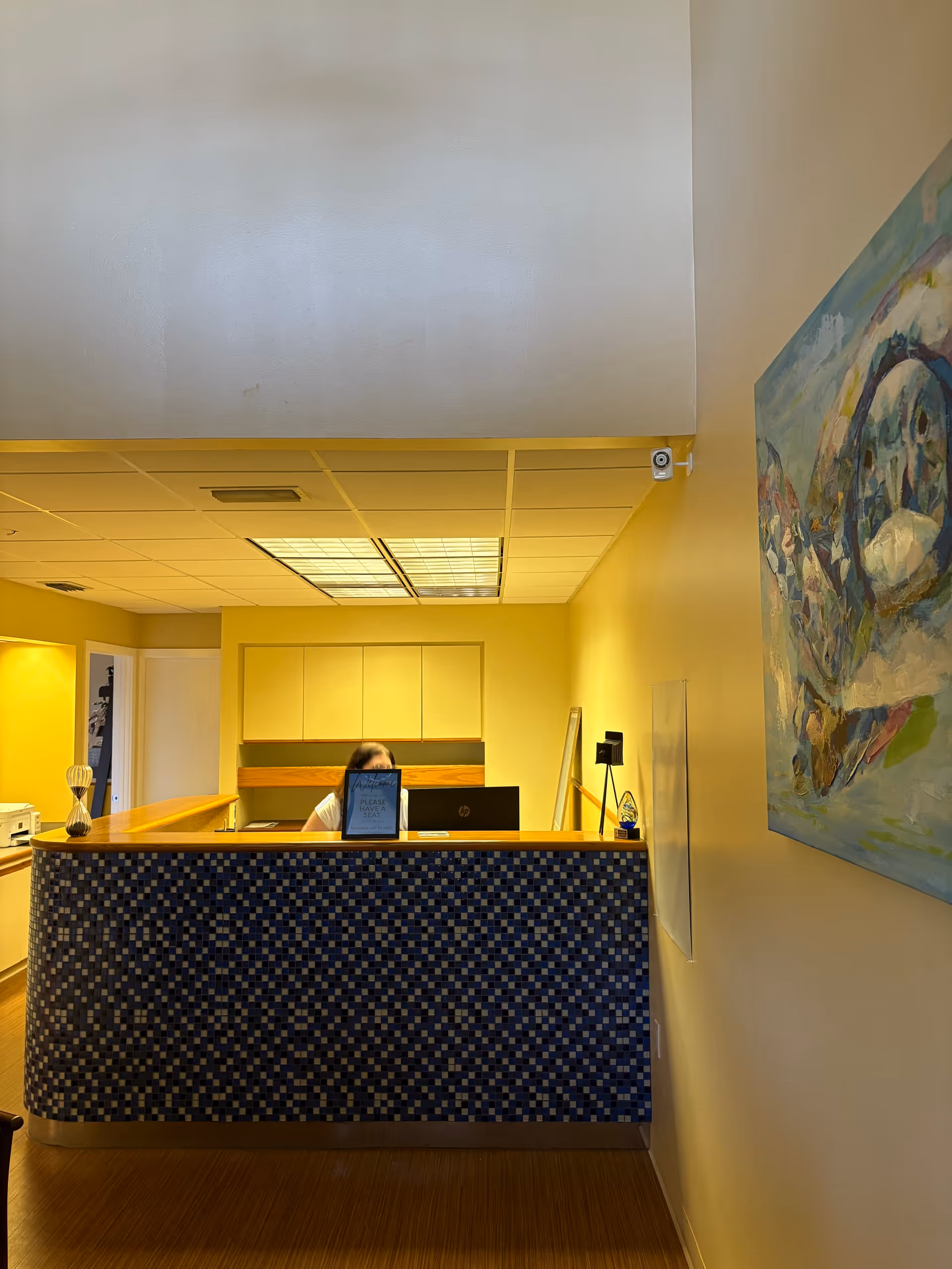 Reception desk in a yellow-walled lobby with artwork, receptionist visible.