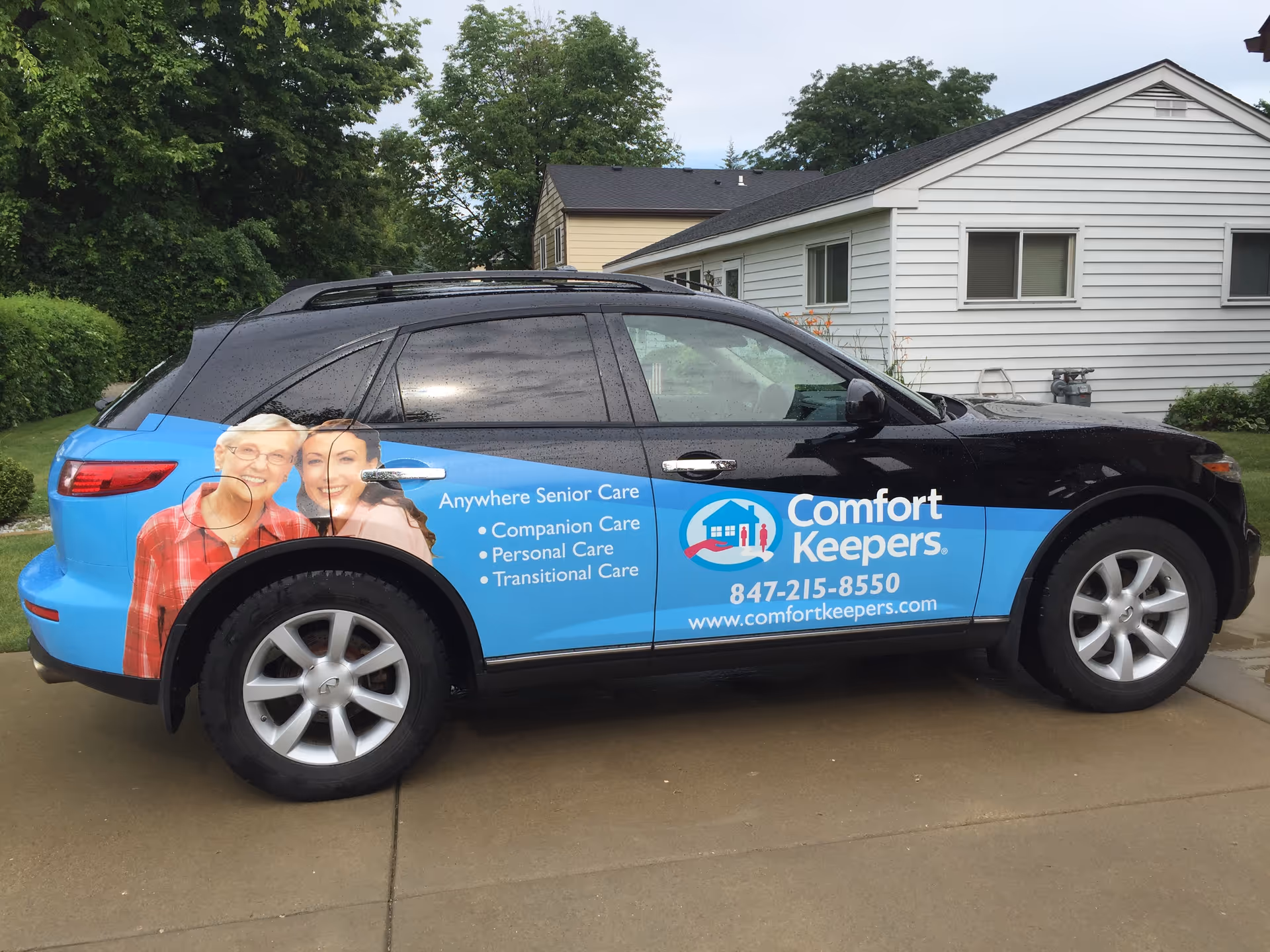 Comfort Keepers branded van parked in a residential driveway beside a white house.