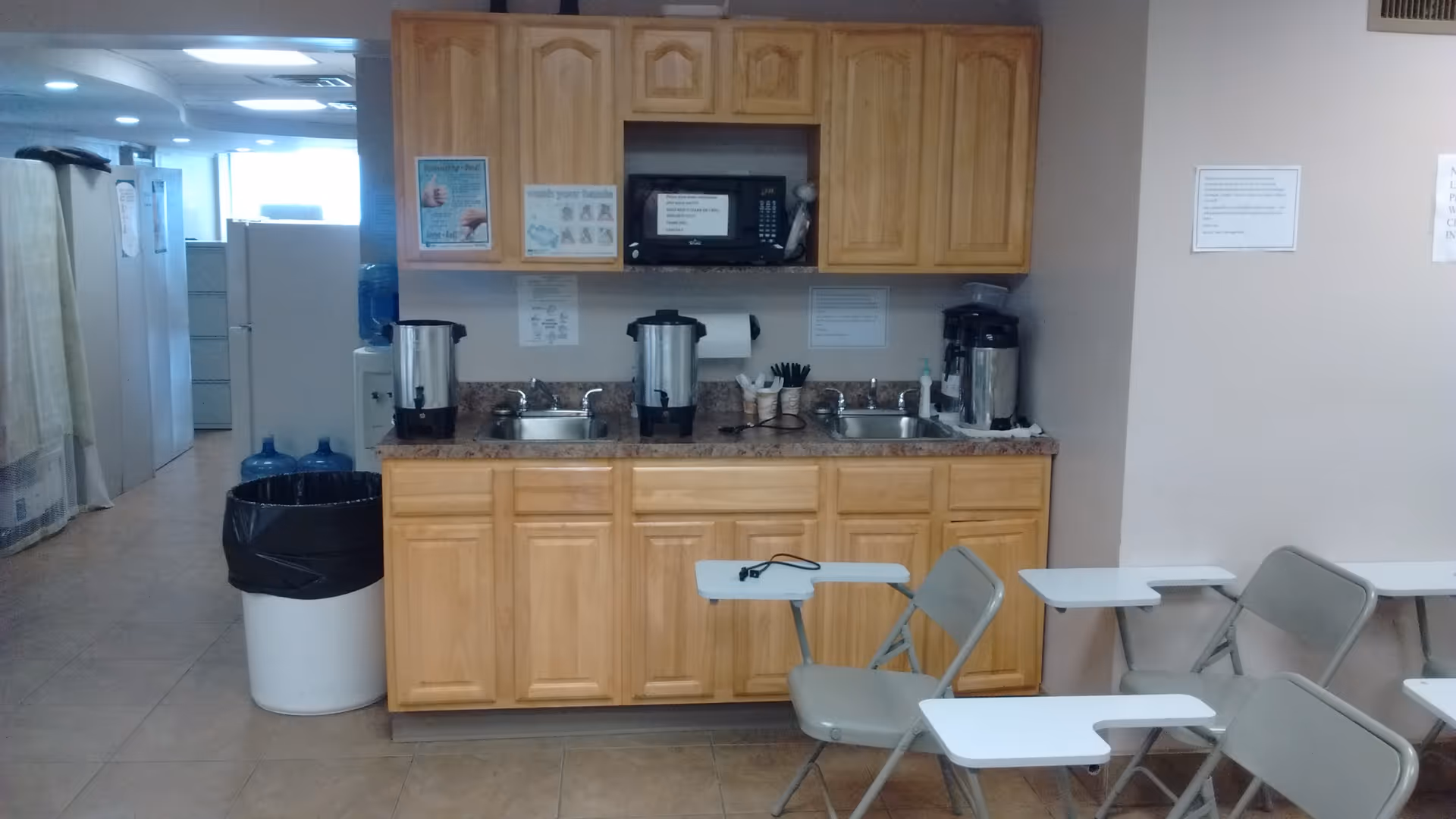 Facility kitchenette with coffee urns, sink, microwave, cabinets, and folding chairs.
