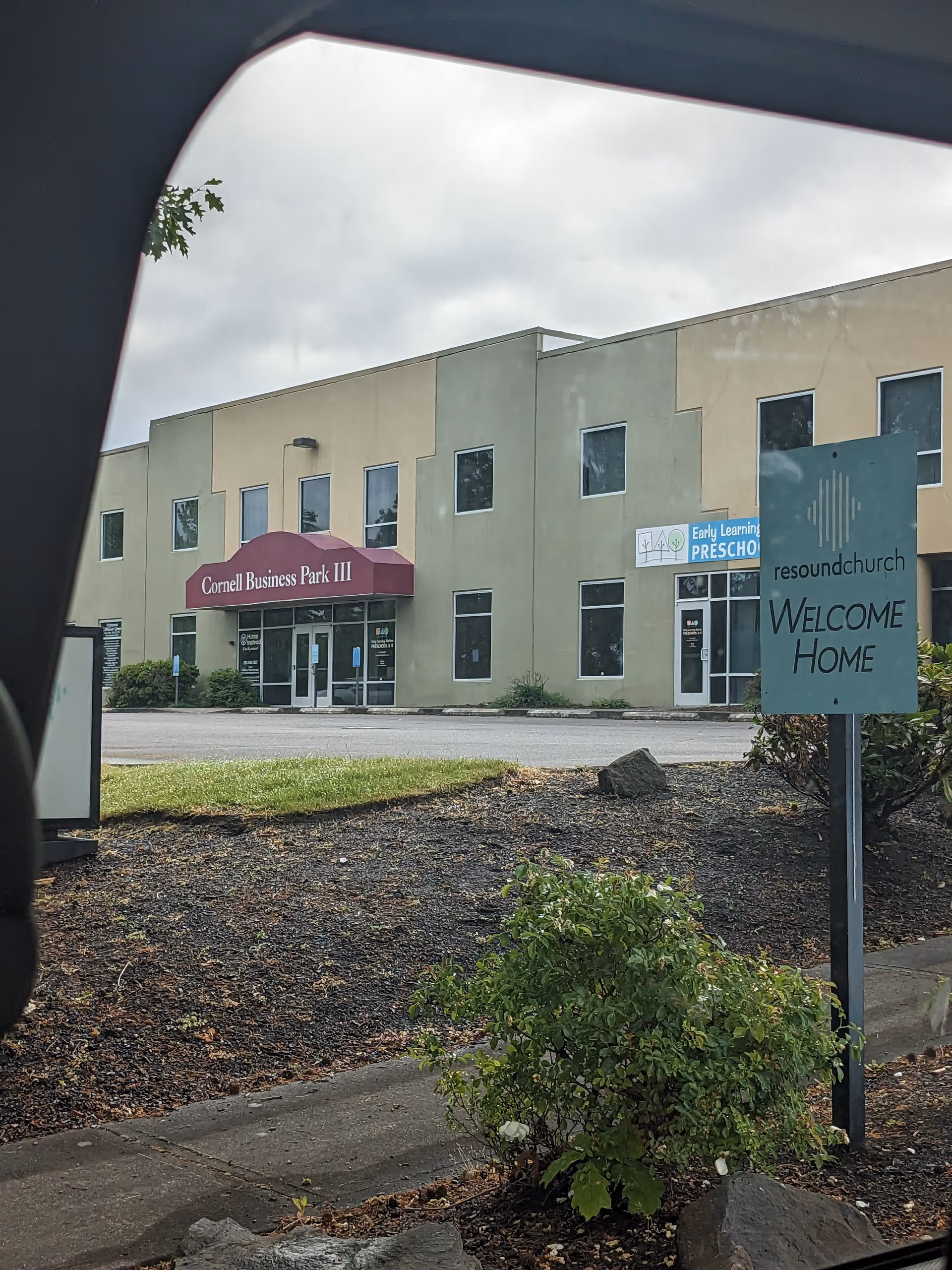 Exterior view of a beige building with storefronts and a Welcome Home sign.