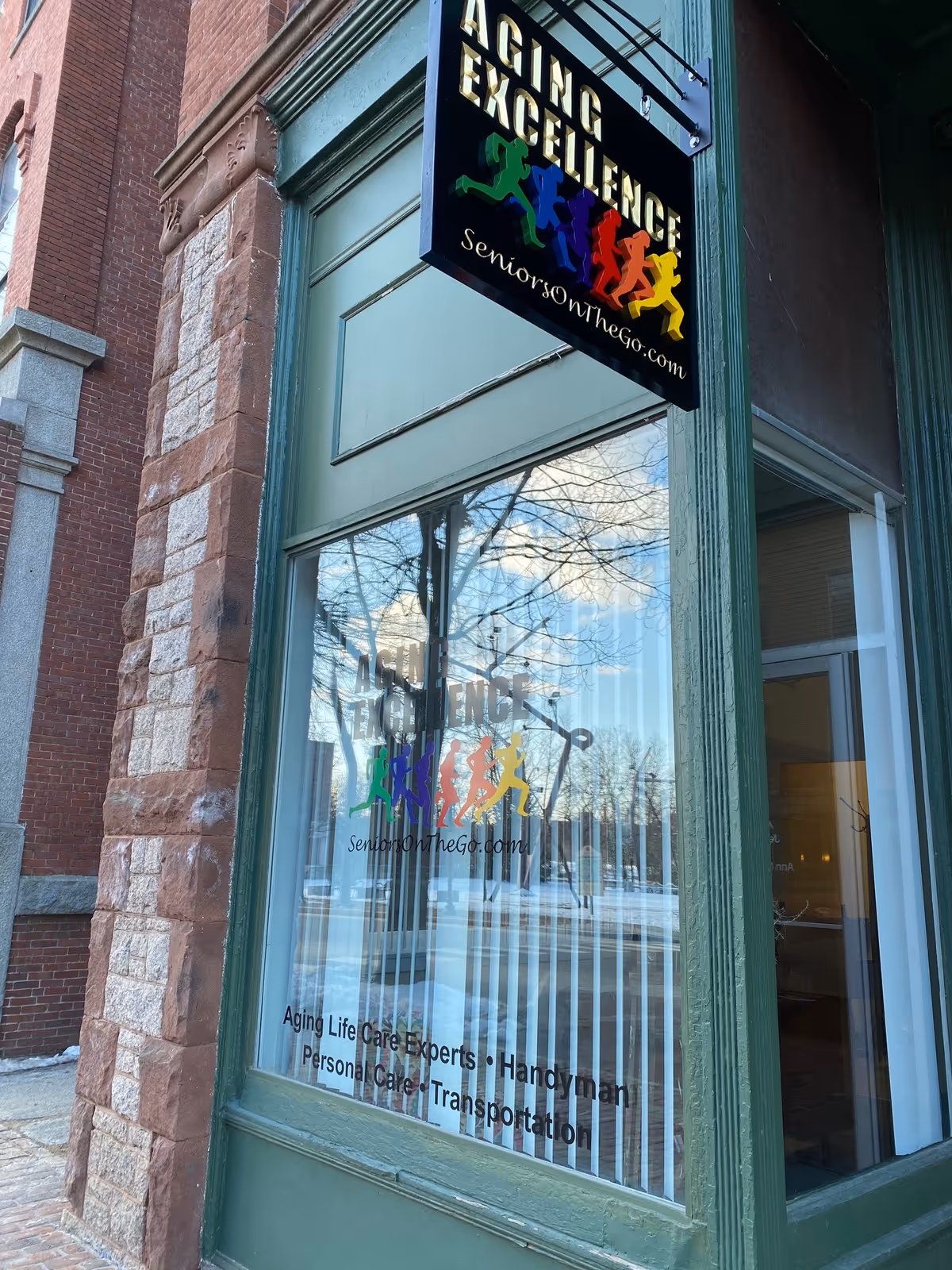 Exterior storefront with Aging Excellence sign and colorful running silhouettes on glass window.