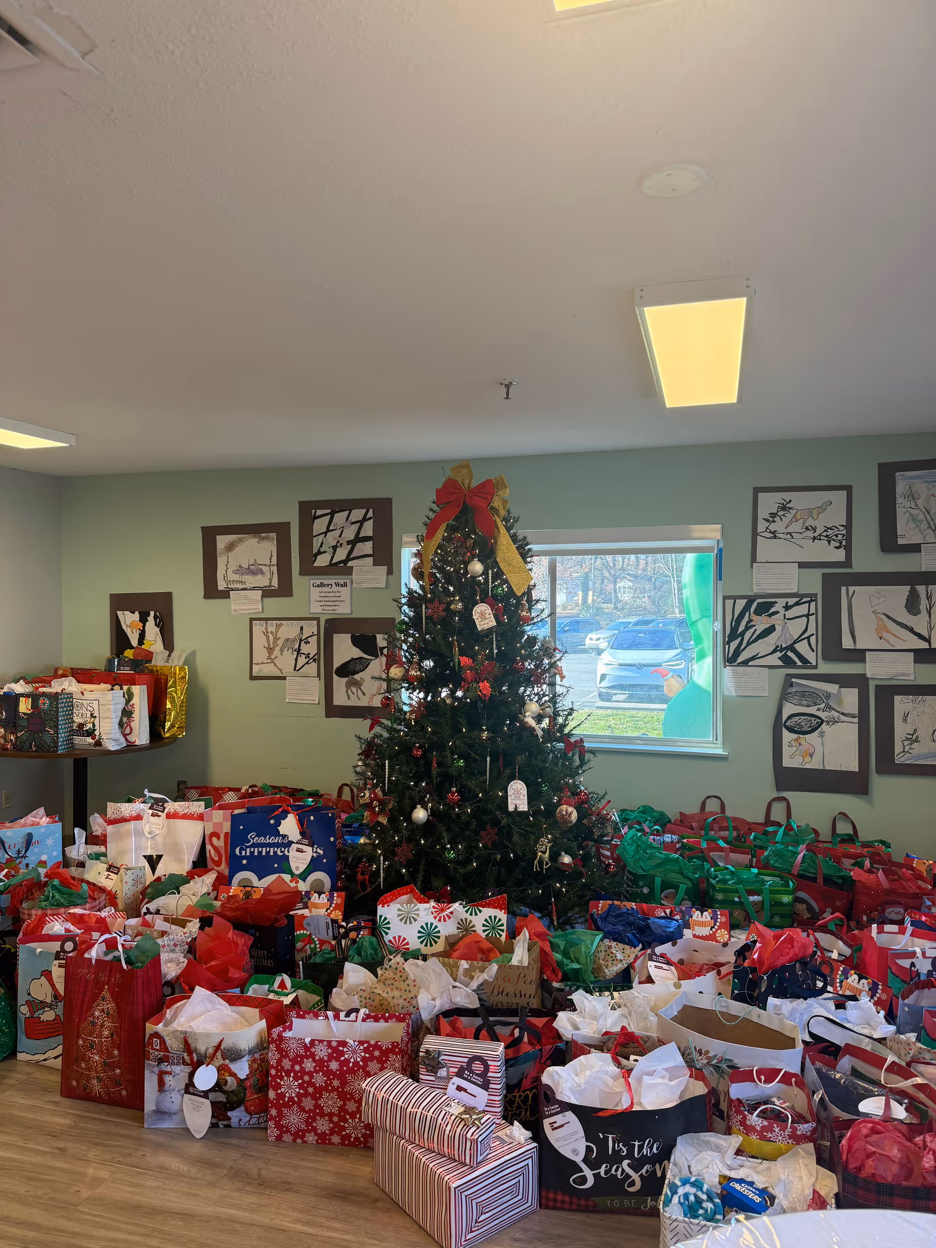 Indoor room with a Christmas tree and many colorful gift bags around it.