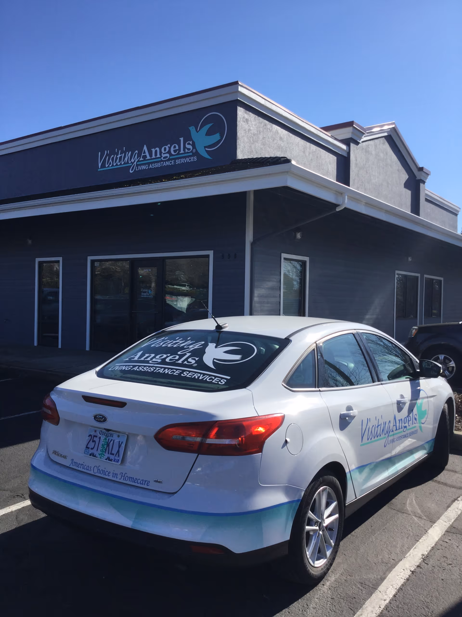 Exterior view of Visiting Angels facility with blue signage and a labeled car in parking.