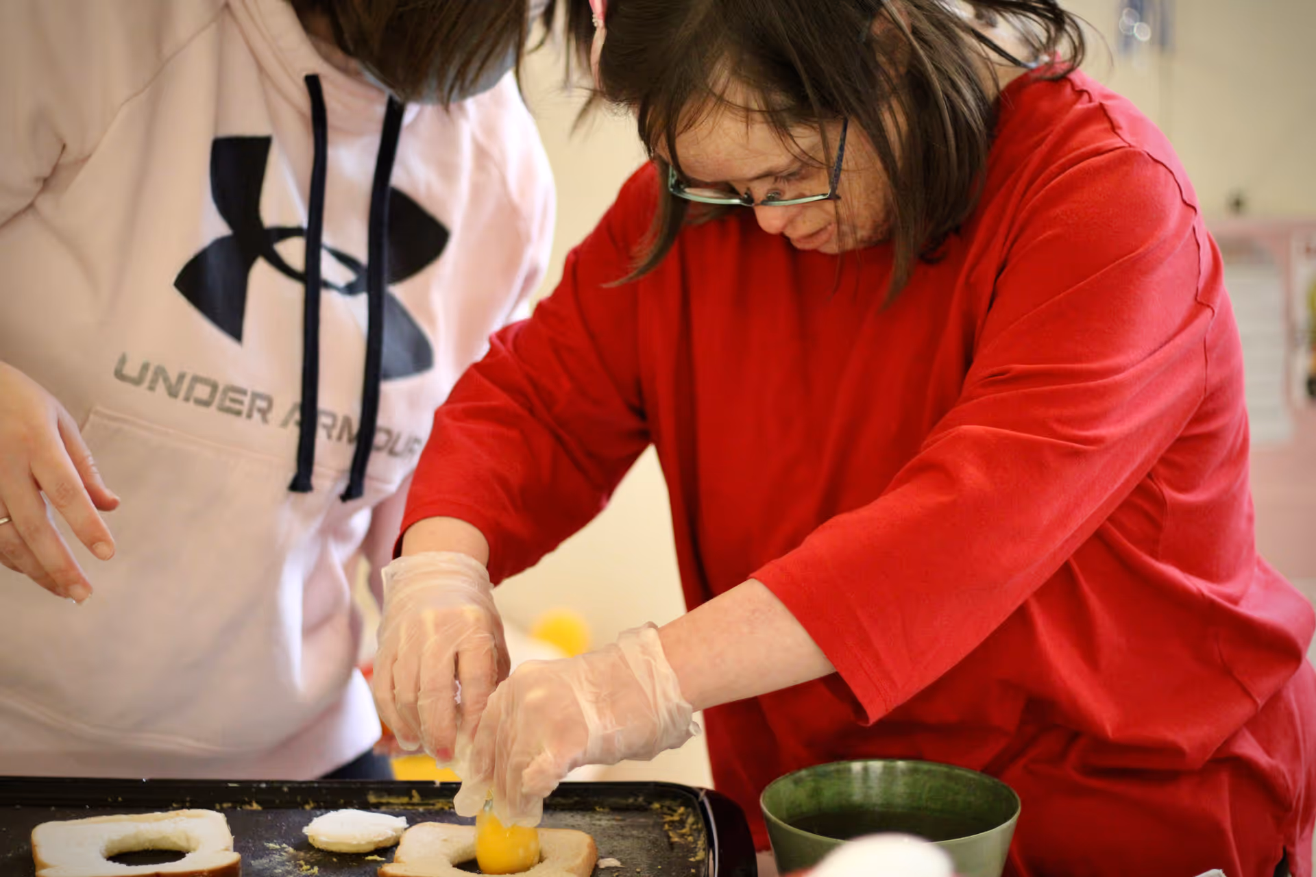 Two people wearing gloves prep dough on a griddle in a kitchen.