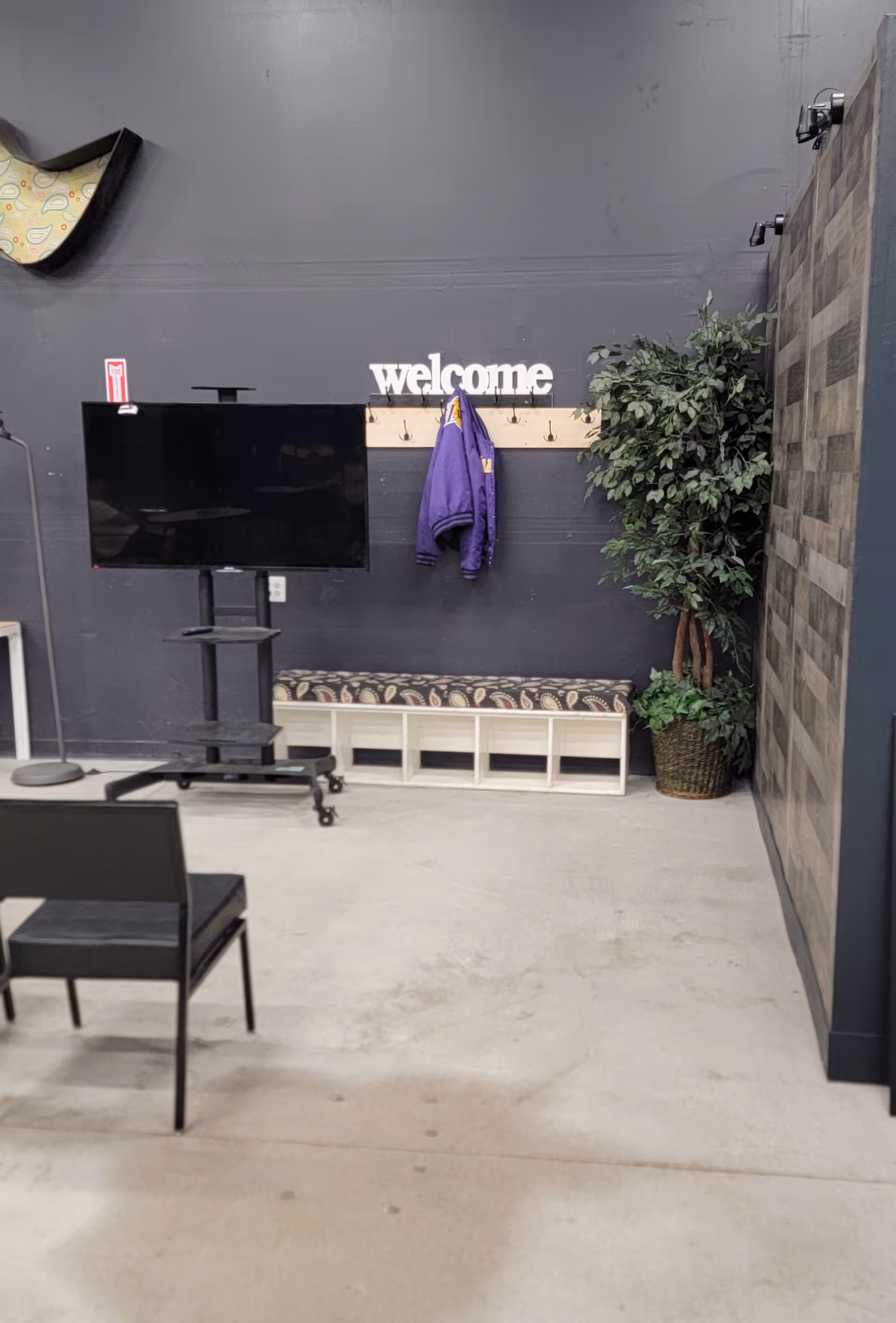 Indoor facility lobby with a welcome sign, coats, bench, TV on a stand, and plants.