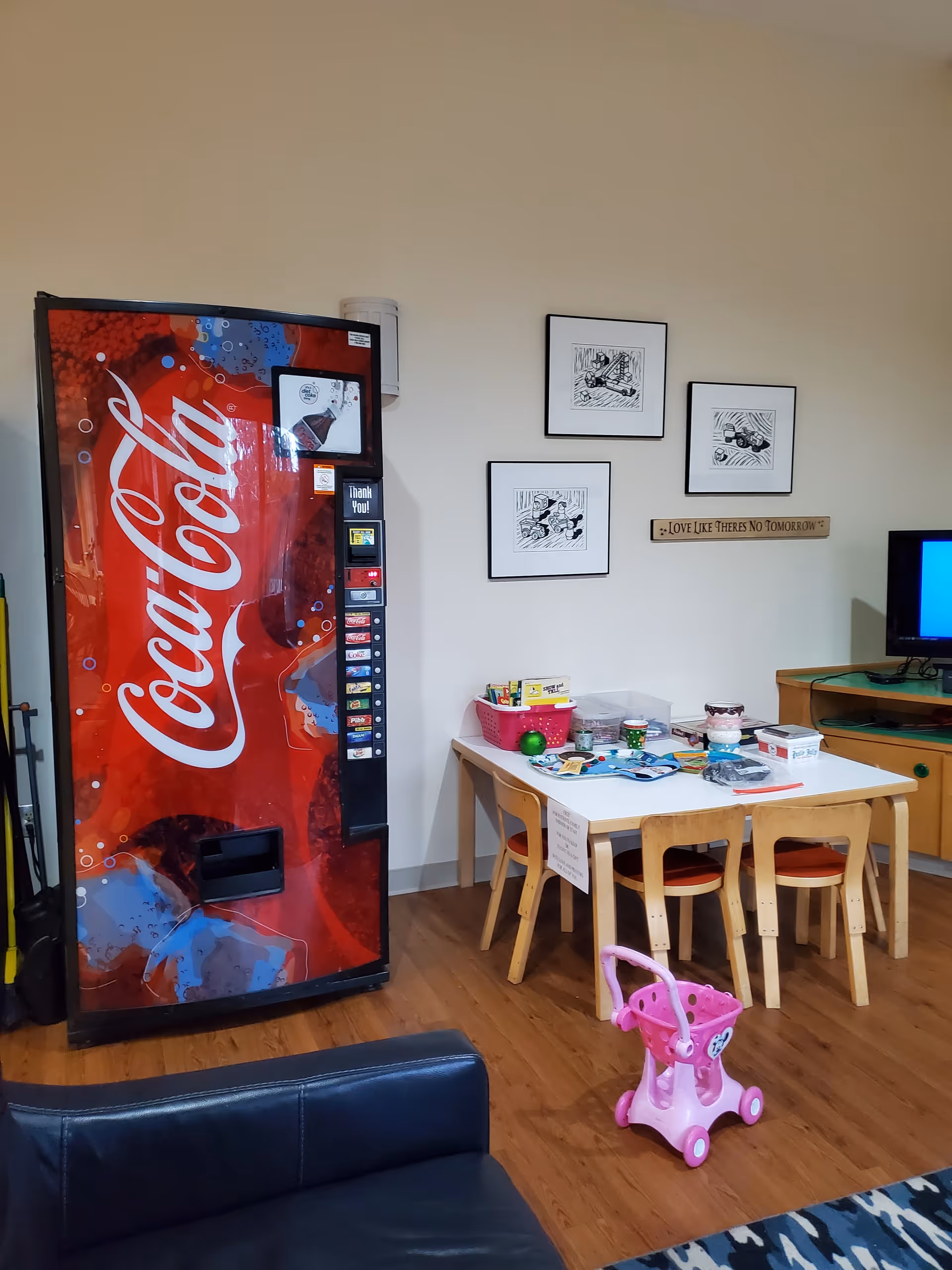 Indoor common area featuring Coca-Cola vending machine, kid-sized table and chairs, toys, and a TV.