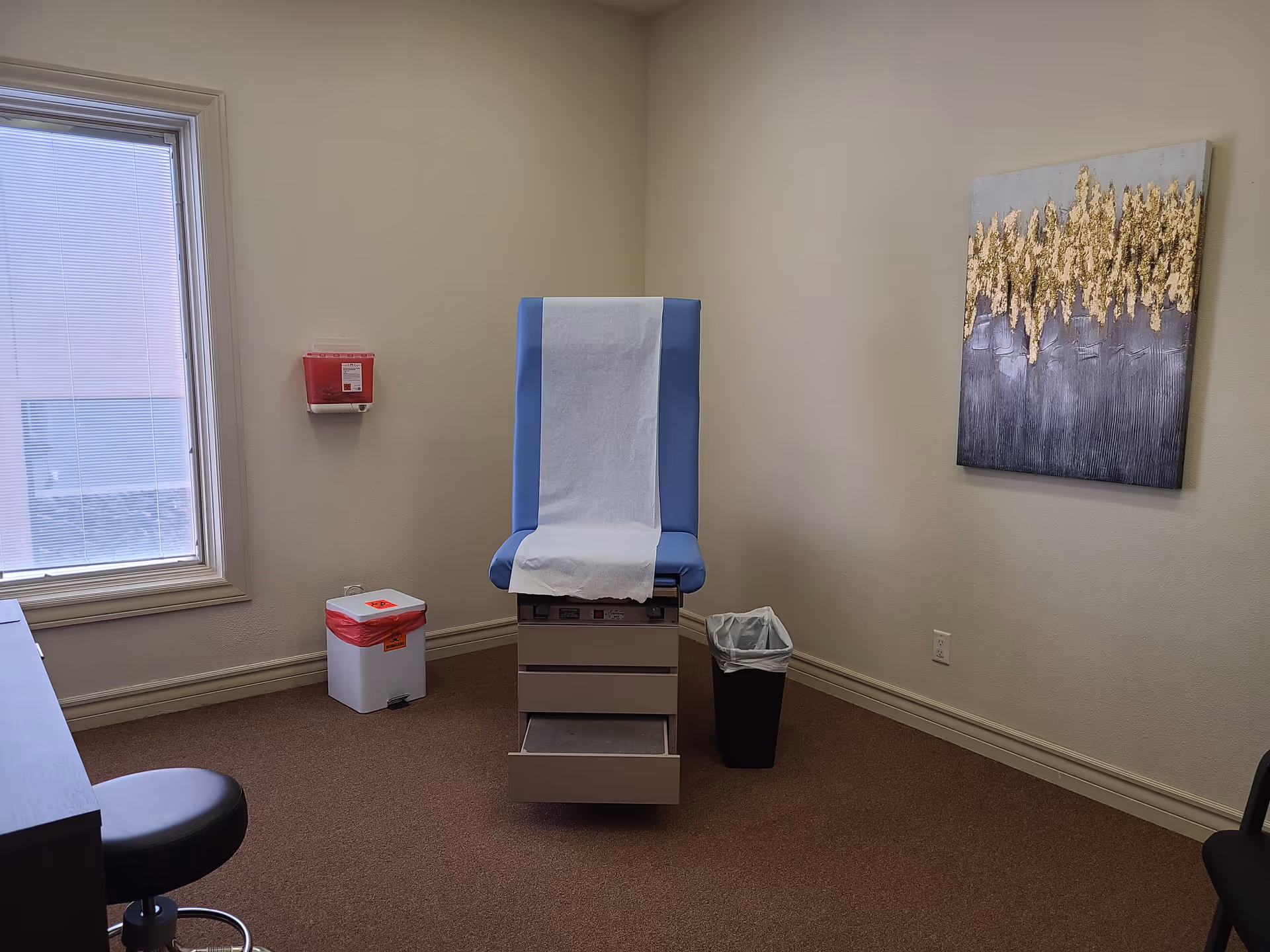 A blue exam chair with disposable paper in a small, empty exam room.