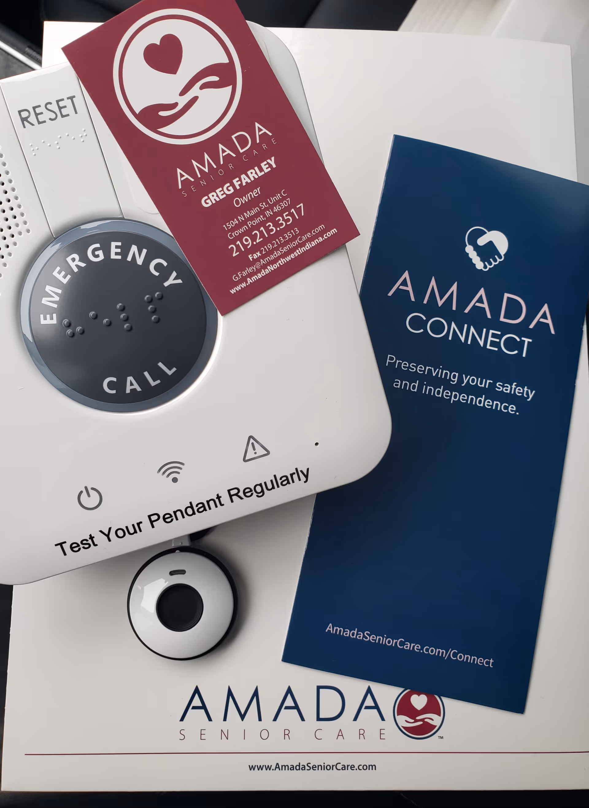 Emergency call device with Amada Senior Care branding and Connect pamphlet on a white surface