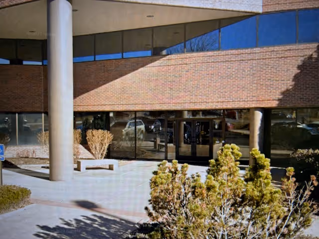 Brick building entrance with glass doors and landscaped front area.