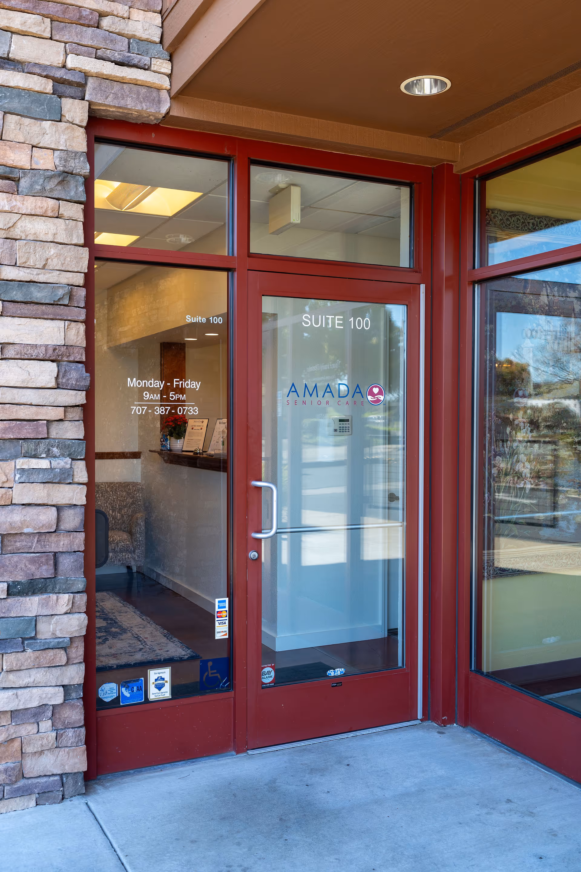Glass entrance door for Amada Senior Care Suite 100, framed by a stone facade.