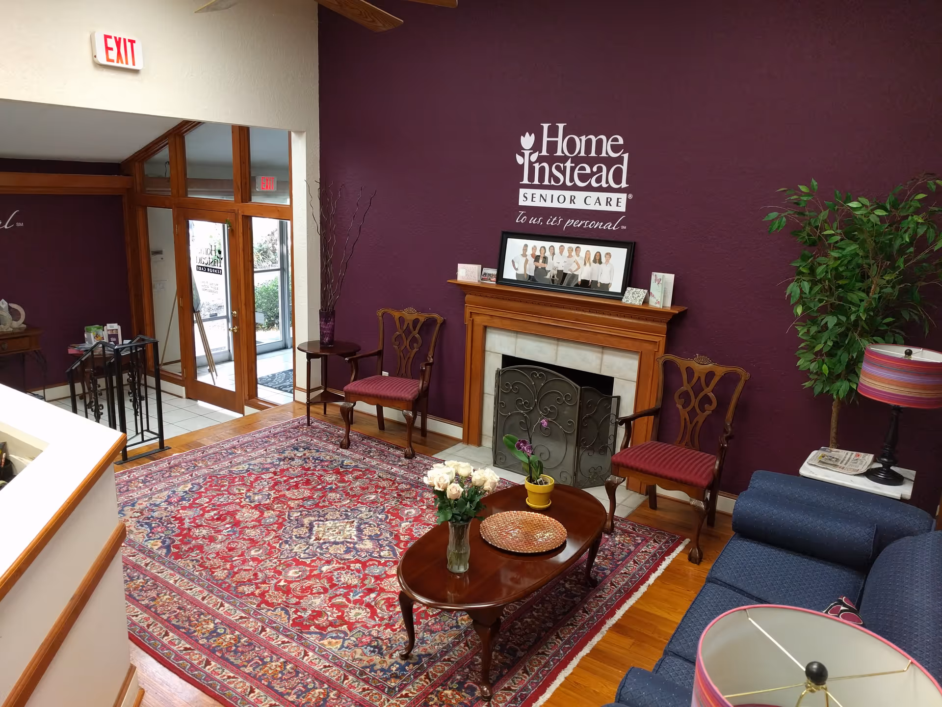Lobby seating area with a purple wall, fireplace, and Home Instead Senior Care logo.
