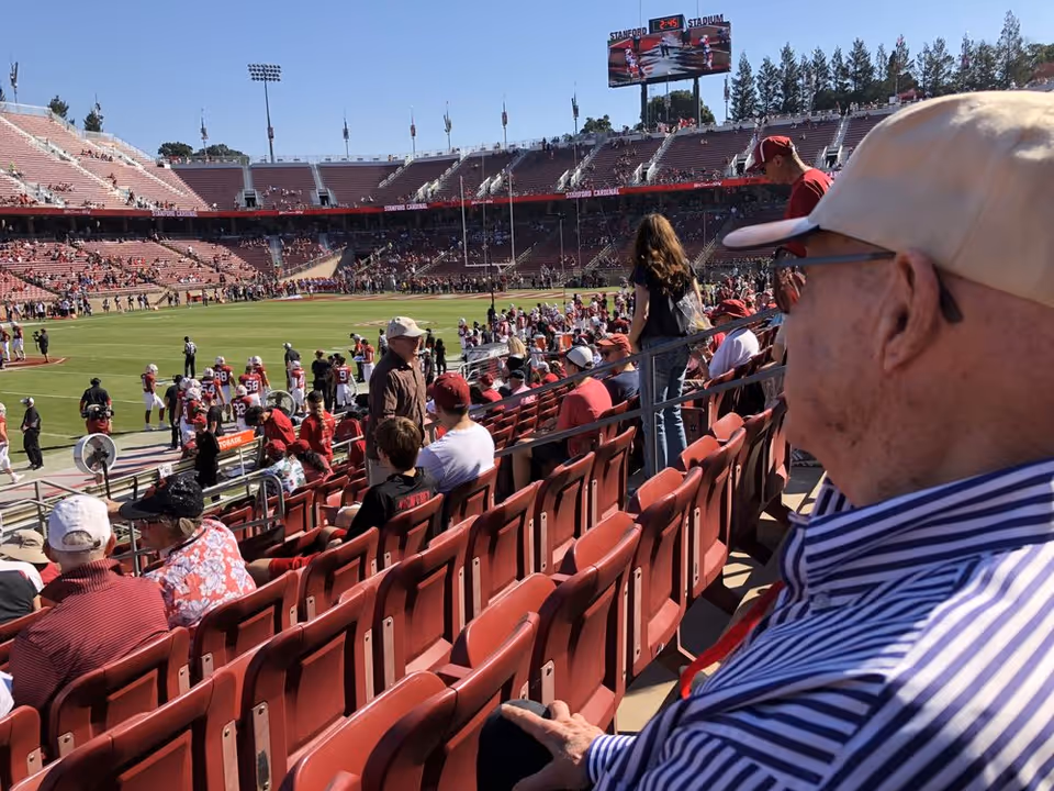 Outdoor stadium filled with spectators seated, watching a football game.