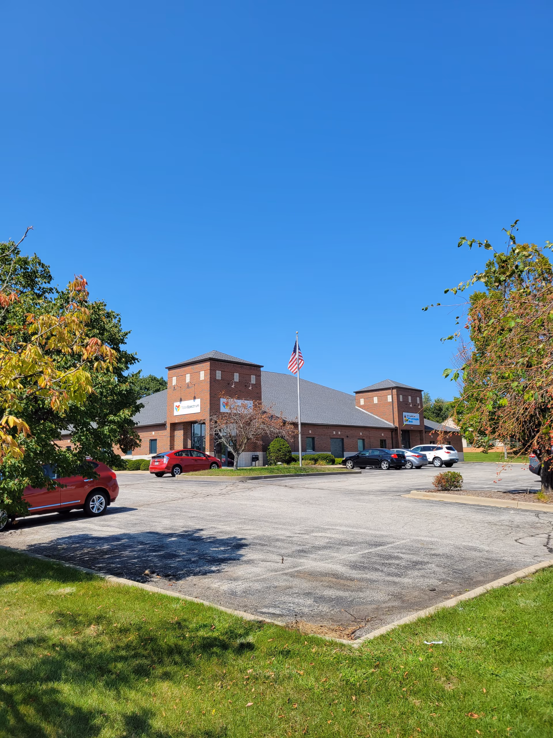 Exterior view of a brick building with parking, trees, and an American flag.
