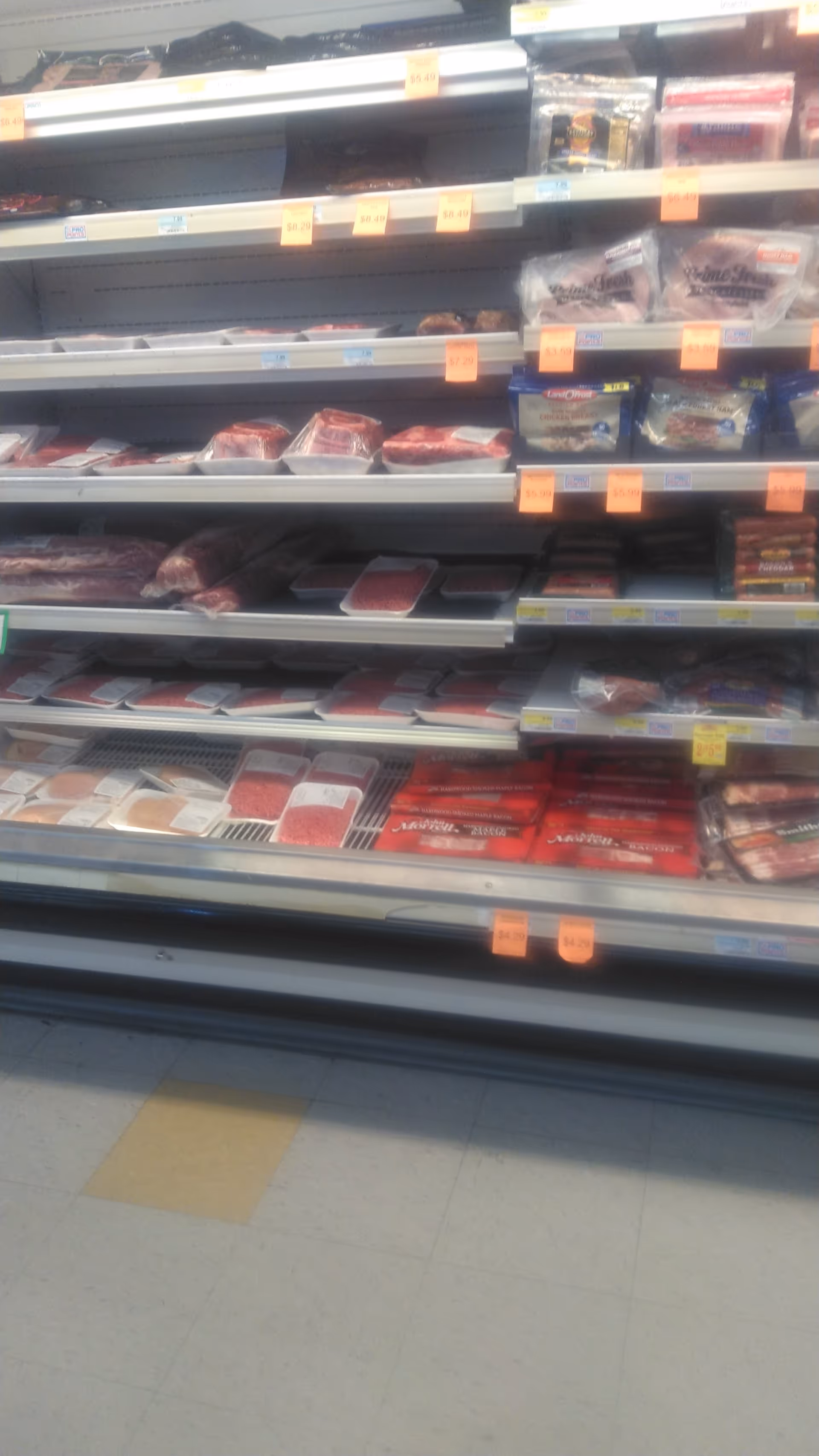 Refrigerated grocery shelves display assorted packaged meats and deli products.