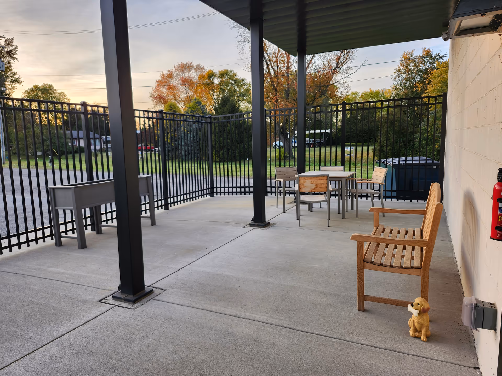 Outdoor patio with railing, tables, chairs, and a small dog statue near the wall.
