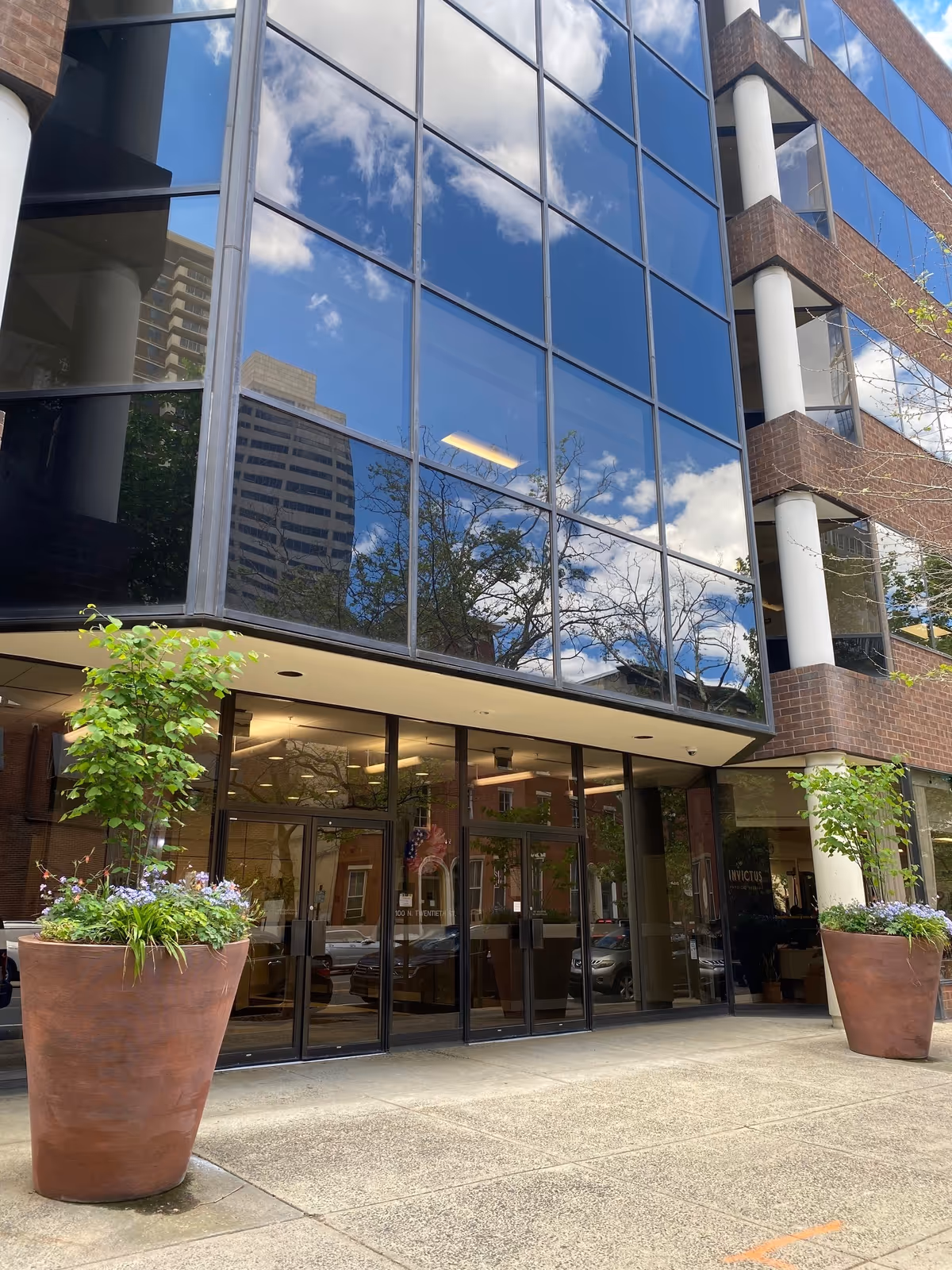 Glass-fronted modern building entrance with tall planters and reflective windows.